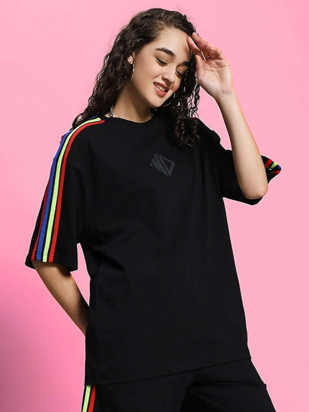 Model wearing black women's oversized t-shirt with rainbow stripes on sleeves, made of premium cotton and elastane blend.