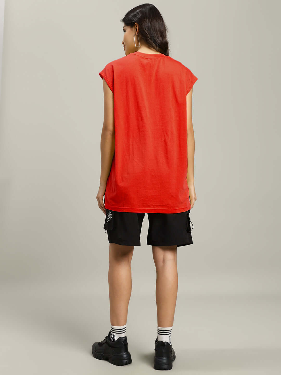Rear view of a woman wearing a red gym t-shirt, black shorts, and black sneakers, emphasizing the casual sporty style.