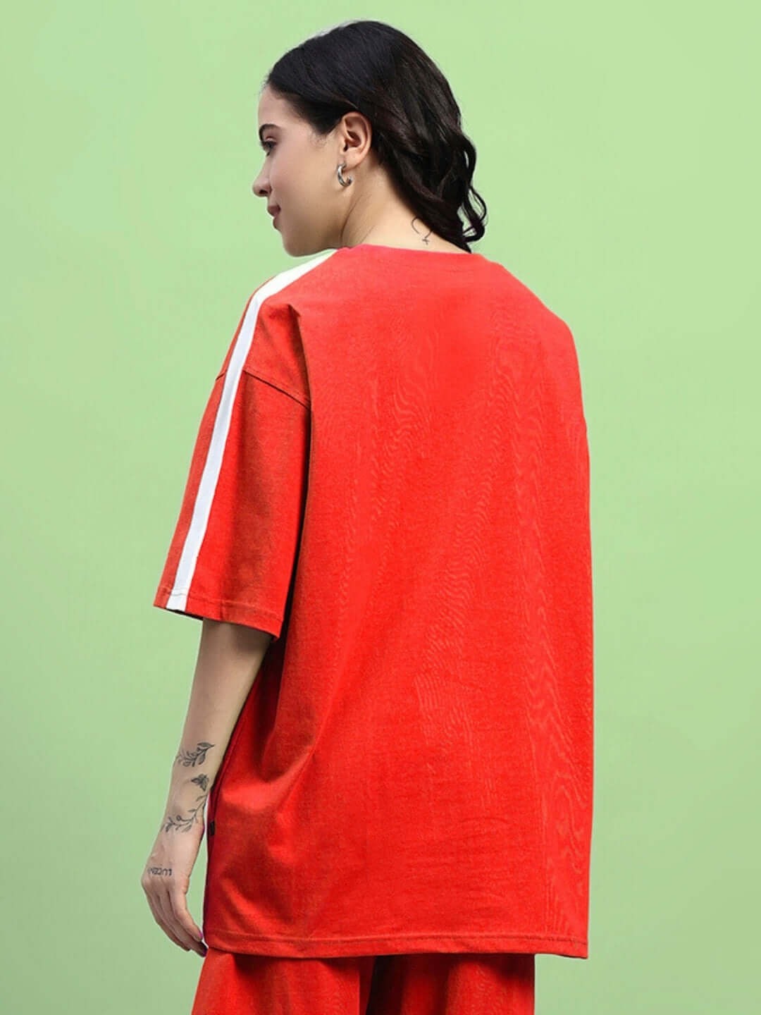 Woman wearing red oversized t-shirt with white stripe on sleeve, made of premium cotton blend, by Color By Colours. Side profile view.