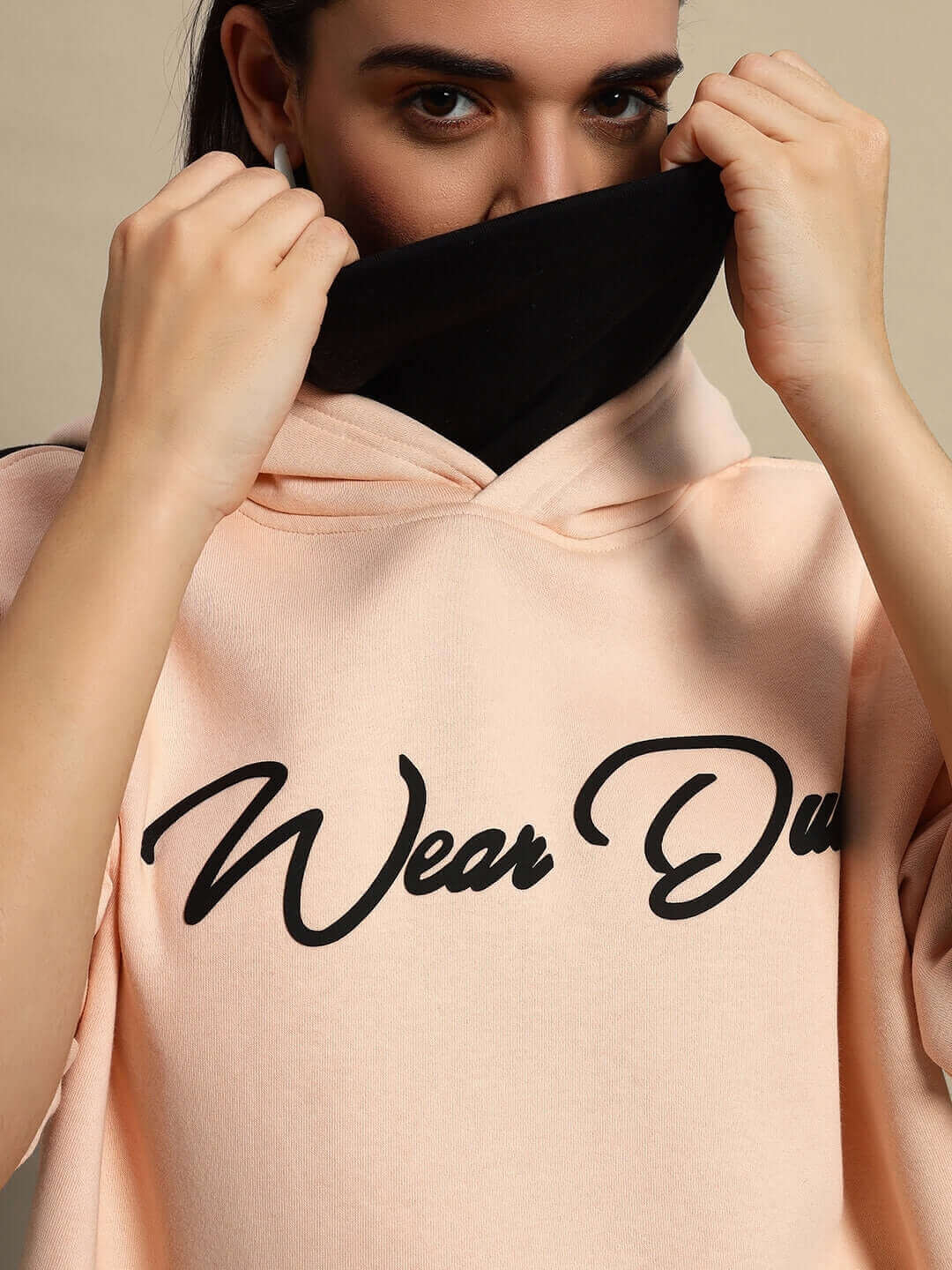 Close-up of a woman wearing a beige-black REGIMENT fleece hoodie, partially covering face, showcasing the 'Wear Du' logo on hoodie.
