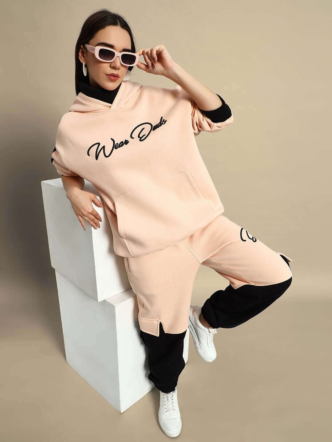 Woman wearing Women's Regiment Fleece Hoodie in beige and black, posing with sunglasses. Stylish casual wear for women.