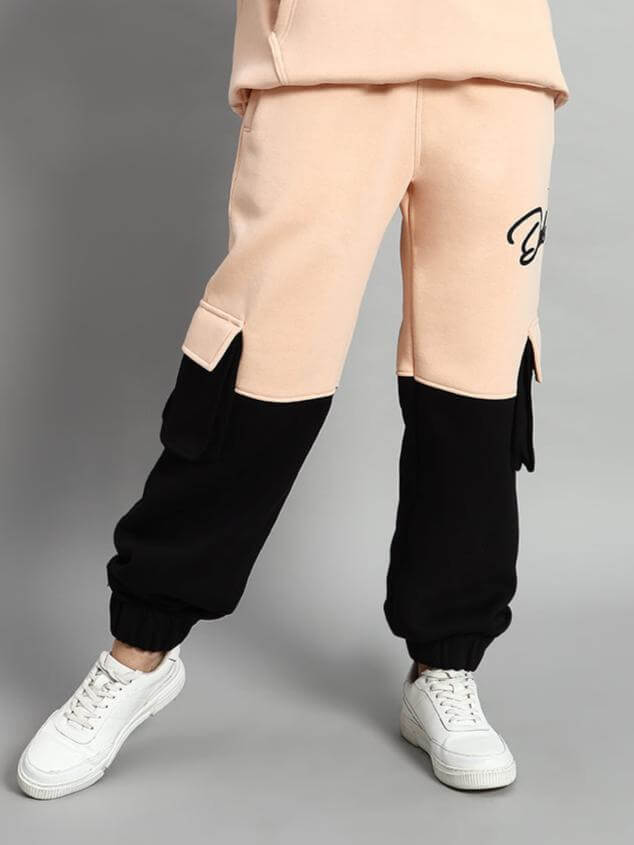 Model wearing WOMEN REGIMENT FLEECE PANT BEIGE BLACK with elastic waistband, ribbed hems, and side pockets, showcasing urban streetwear style.