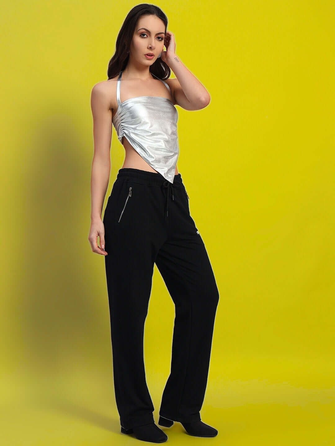 Woman wearing WOMEN'S REGIONAL CROP TOP SILVER with black pants, showcasing sleek modern design against a bright yellow background.