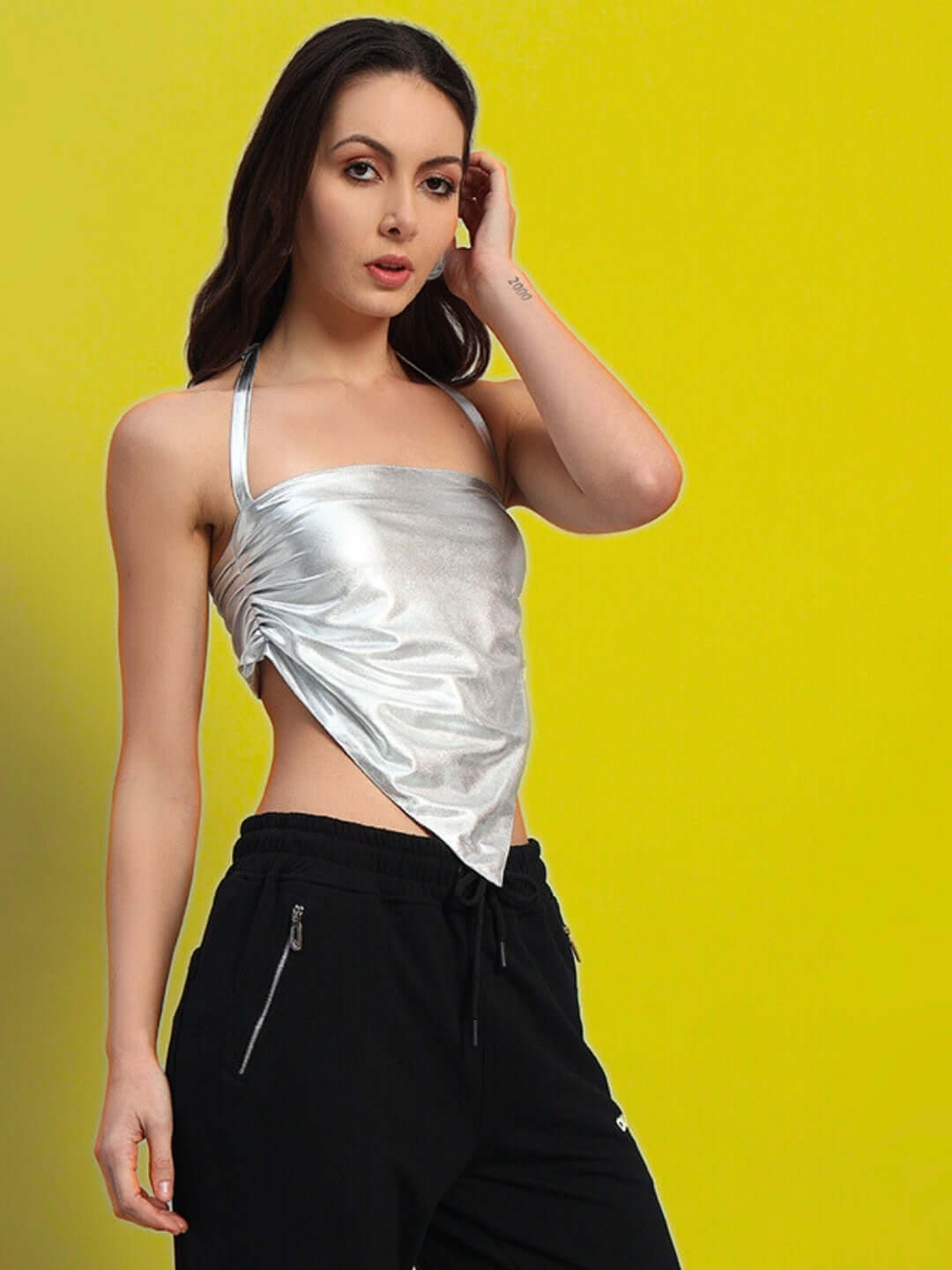 Model wearing a women's silver metallic crop top from Color By Colours, styled with black pants, featuring halter neck design.