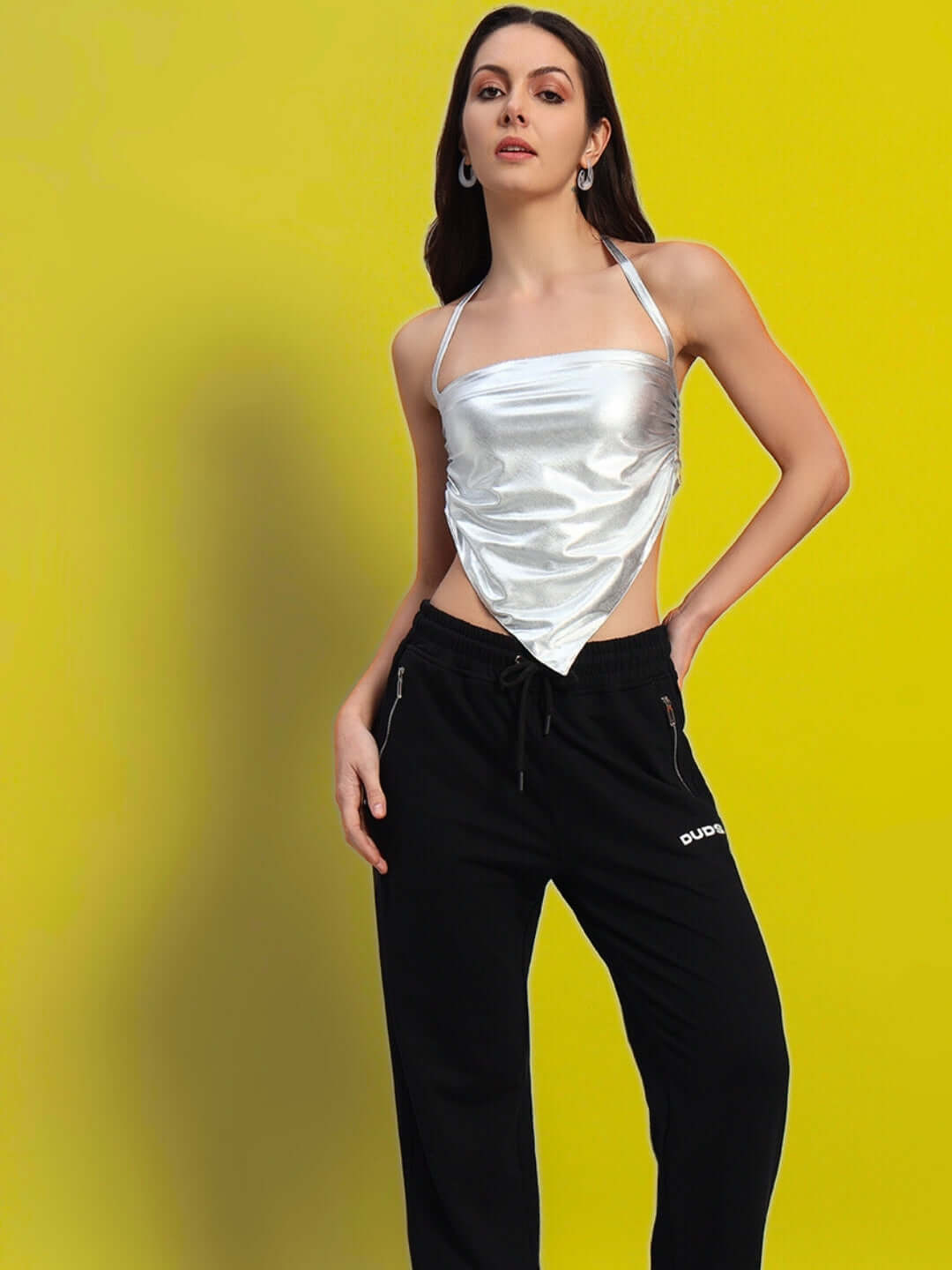 Woman modeling silver metallic crop top with black pants against a yellow background.