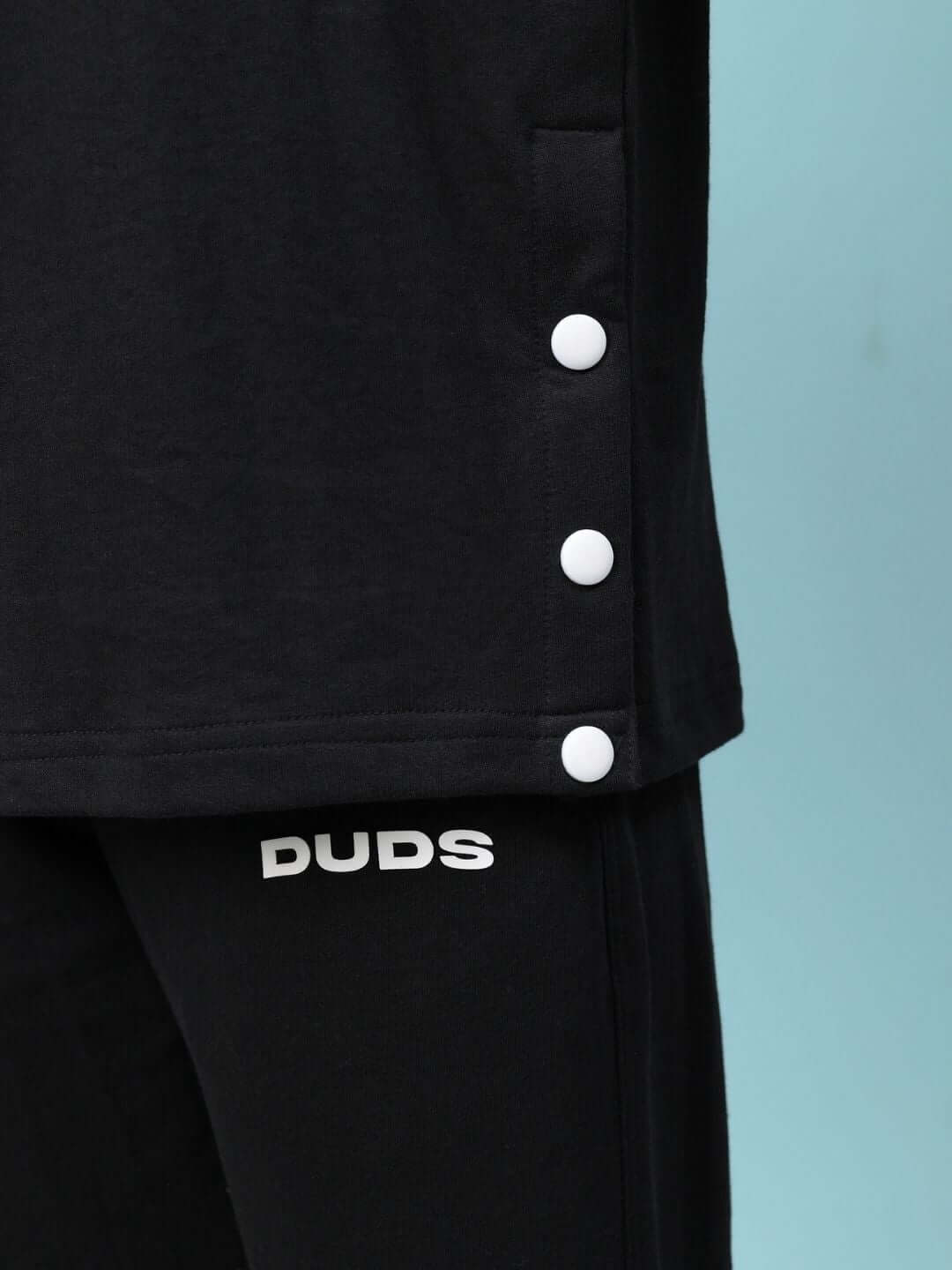Close-up of WOMEN'S WESENT RELAXED-FIT CO-ORD SET BLACK with button details and logo on pants, made from premium cotton and elastane.