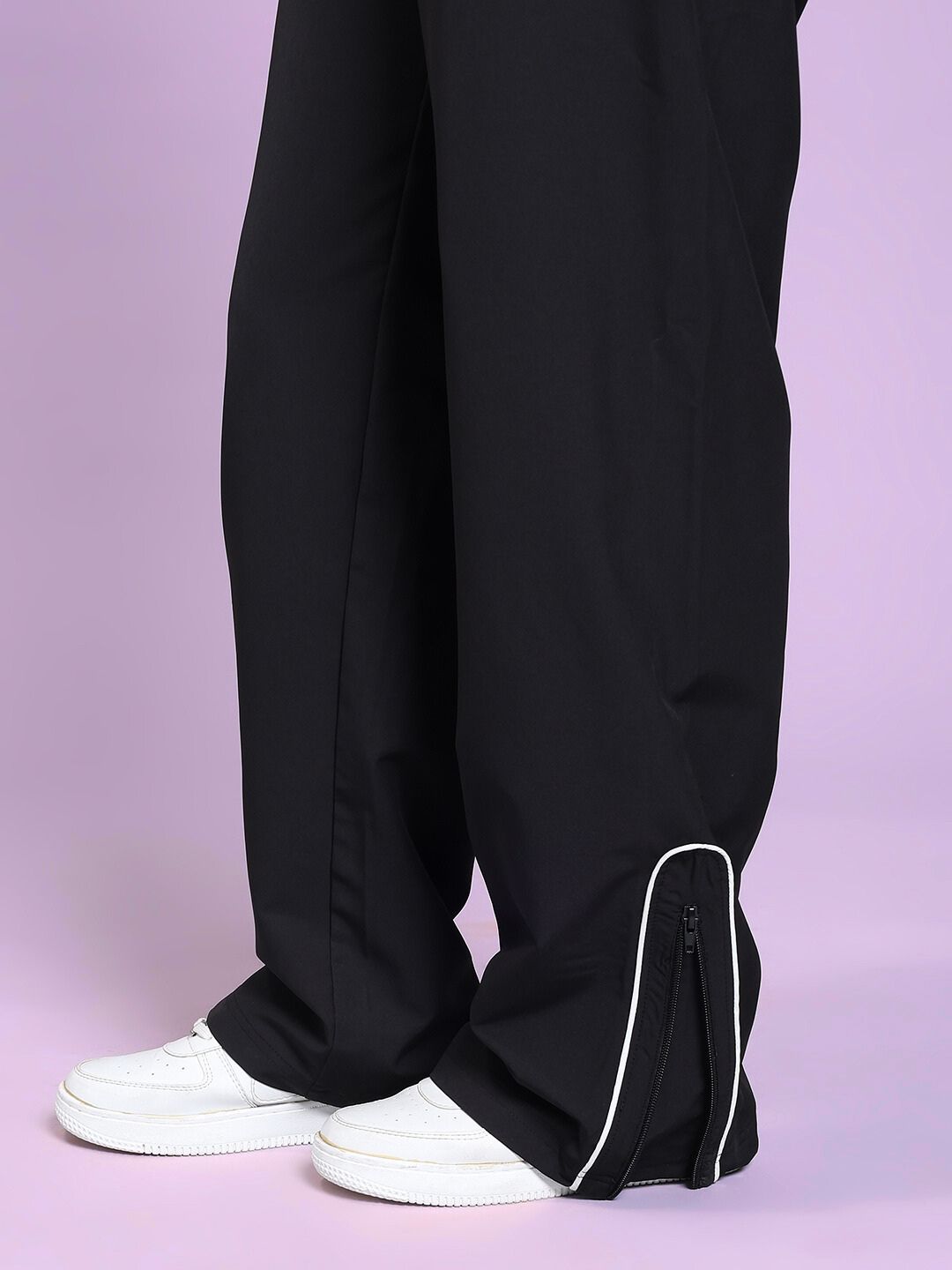 Close-up of WOMEN PERFACT RELAXED-FIT JOGGER BLACK with zippered cuffs and sneakers on a pastel background.