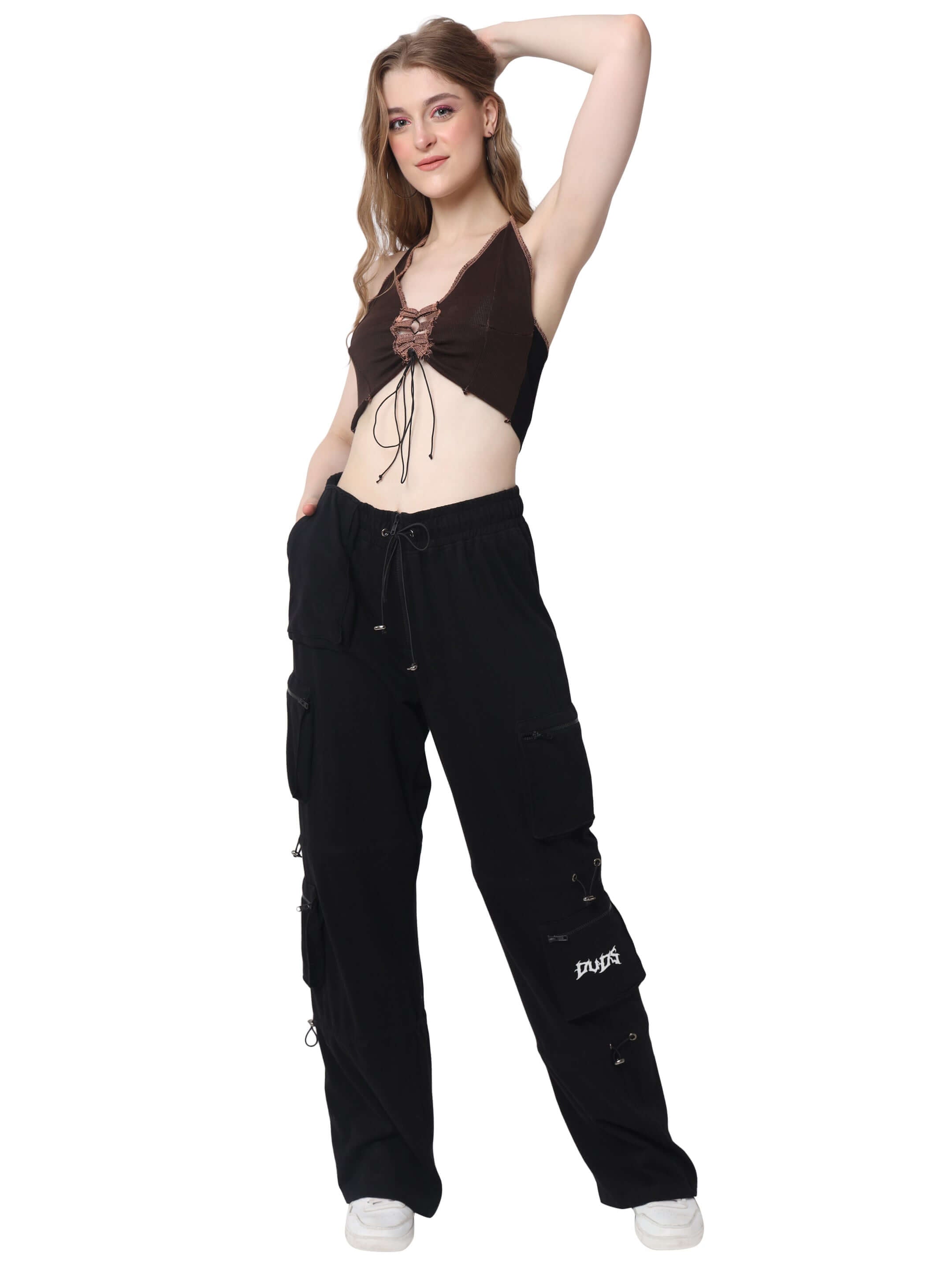 Woman wearing a brown ribbed crop-top and black cargo pants, styled with white sneakers, posing confidently.