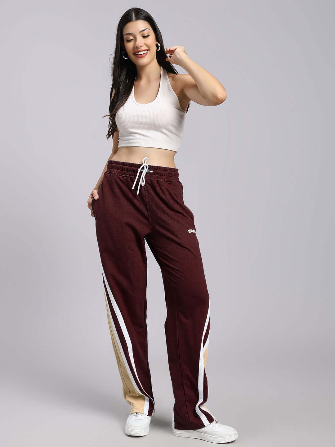 Woman wearing maroon relaxed fit joggers with side stripes, paired with a white tank top and sneakers.