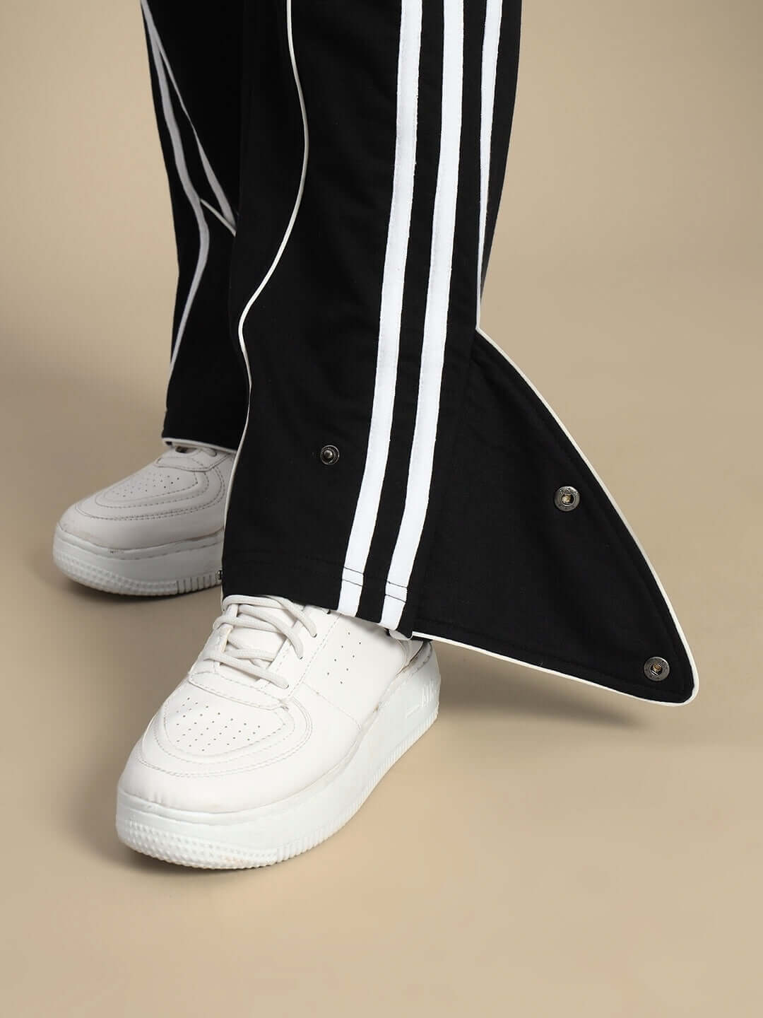 Black women's joggers with white stripe detail and snap buttons, paired with white sneakers for a stylish casual look.