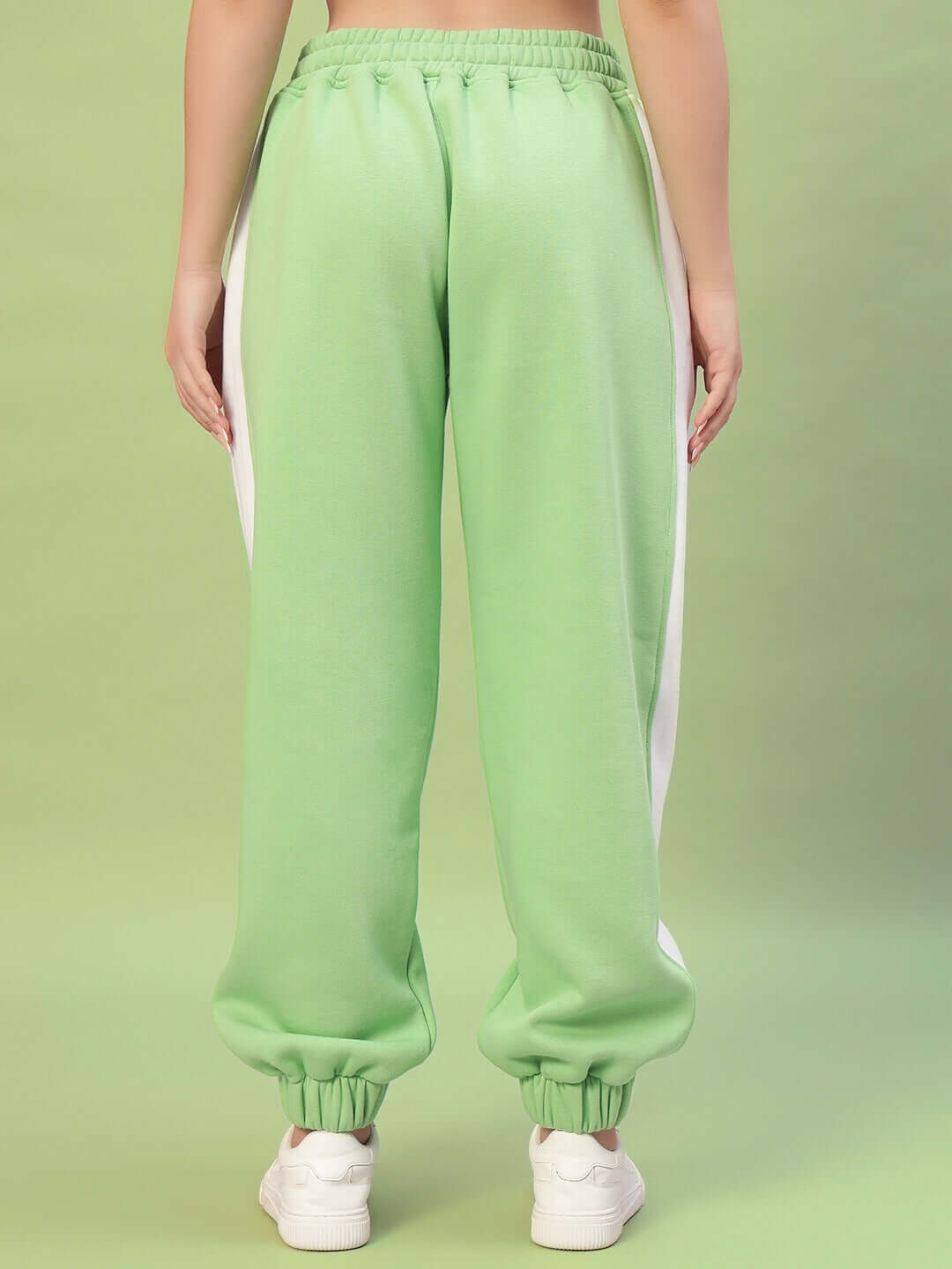 Woman wearing WOMEN RIZZLER FLEECE COLORBLOCK JOGGER GREEN, showcasing vibrant colorblock design from back view on green background.