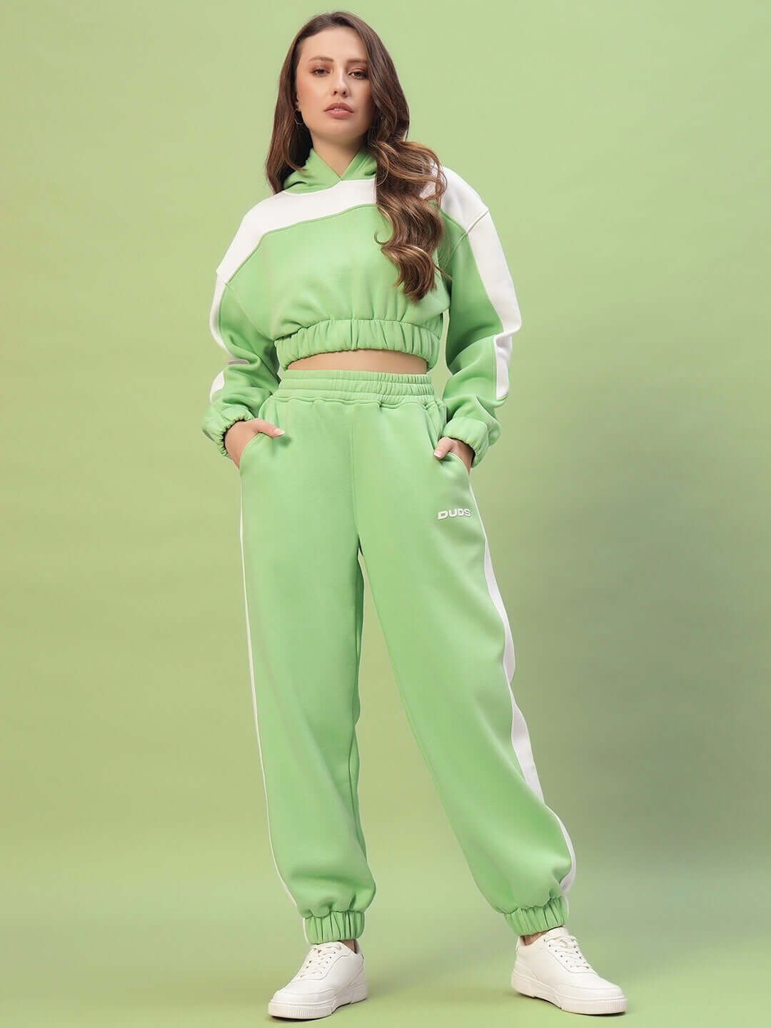 Woman wearing WOMEN RIZZLER FLEECE COLORBLOCK JOGGER GREEN with matching hoodie, styled with white sneakers against a green background.