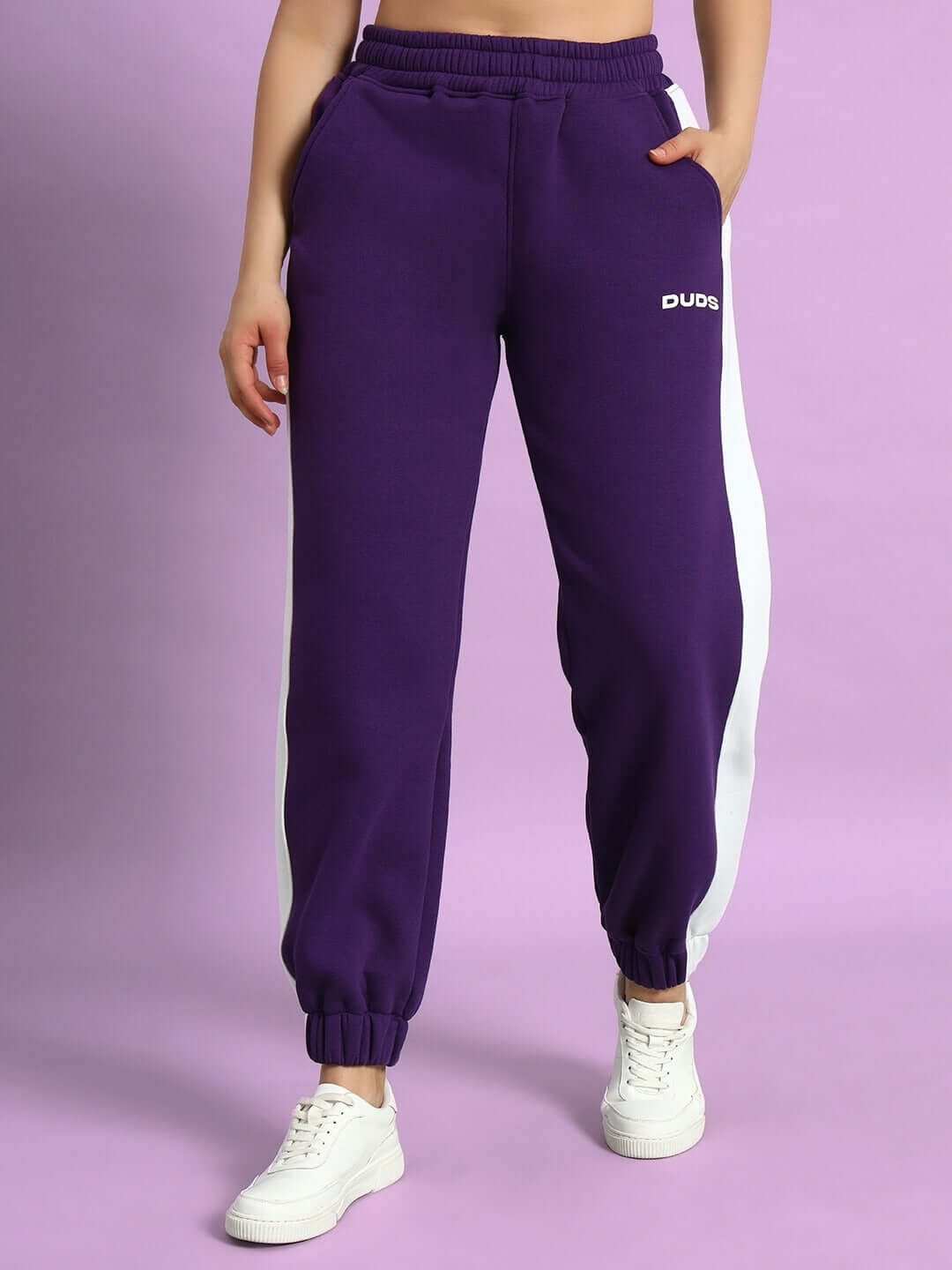 Woman wearing WOMEN RIZZLER FLEECE COLORBLOCK JOGGER PURPLE with white sneakers, showcasing stylish purple joggers.