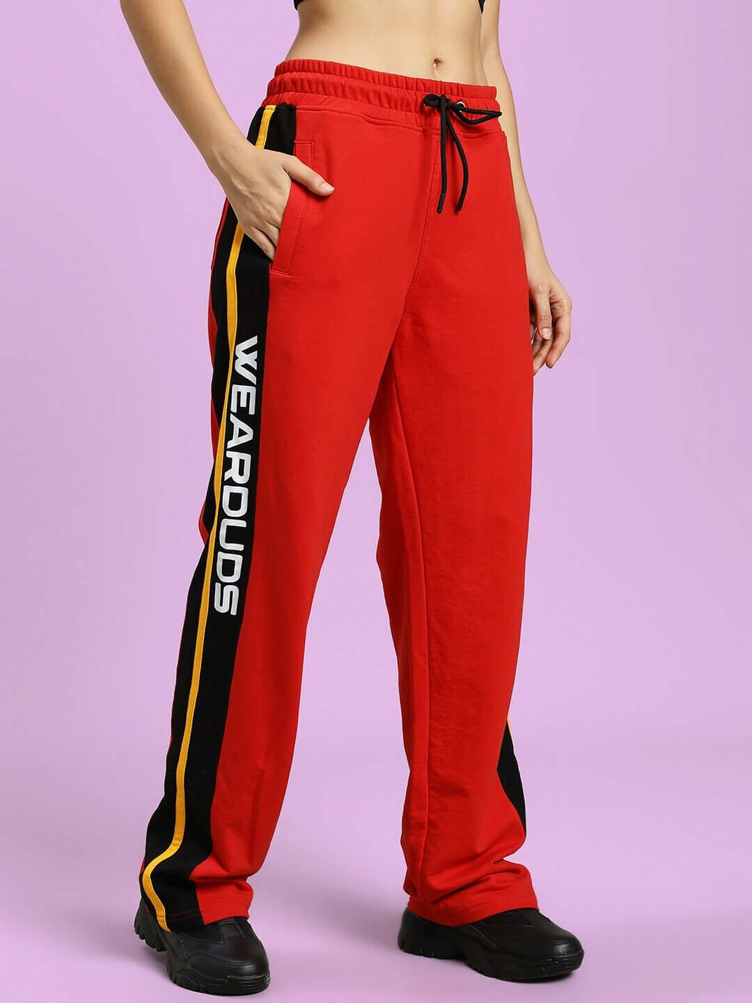 Model wearing WOMEN'S ROGER RELAXED-FIT JOGGERS RED with side pockets and black drawstring, showcasing casual style on purple background.