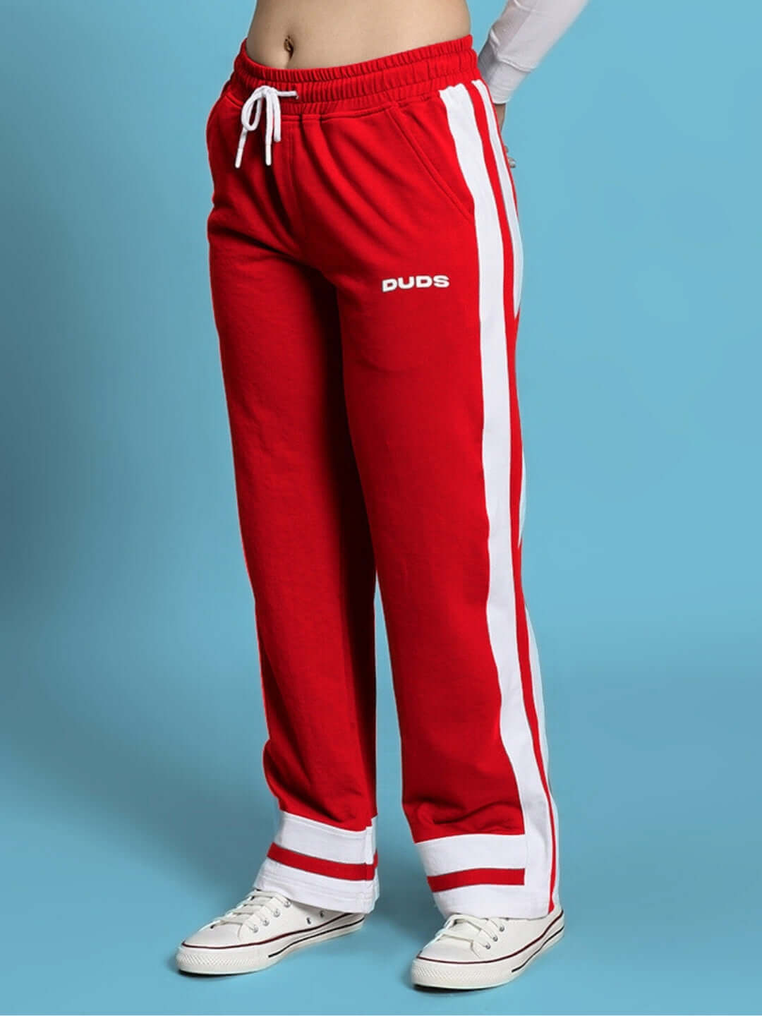 Red women's jogger with side stripe, DUDS brand, worn with white sneakers, on blue background.