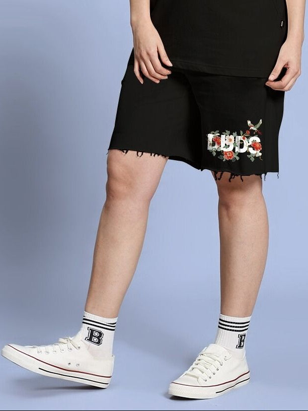 Person wearing WOMEN ROSE CHARM RELAXED FIT SHORTS BLACK with floral embroidery standing against a blue background.