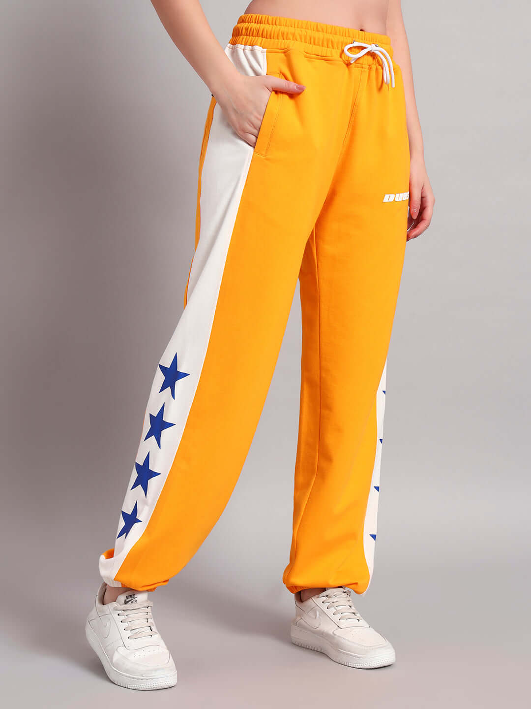 Model wearing women's orange-white relaxed fit joggers with star pattern by DUDS, featuring an adjustable drawstring waist and side pockets.
