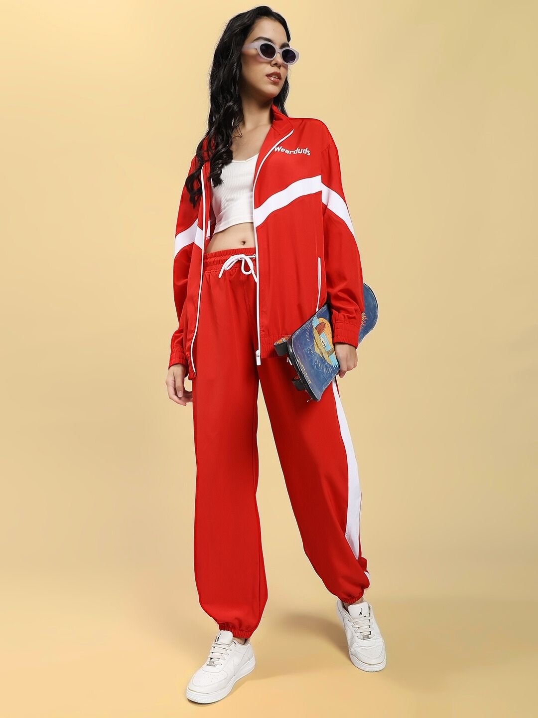 Woman wearing WOMEN ROYAL COMFORT RELAXED FIT CO-ORD SET RED with white sneakers and sunglasses, holding a clutch, stands against a beige background.