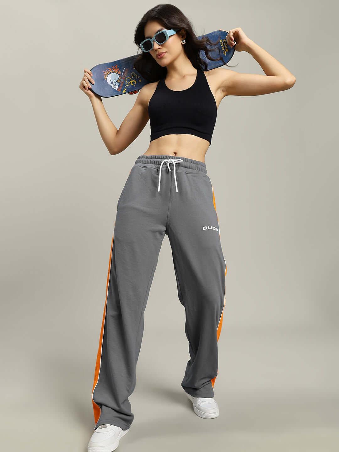 Woman in grey Sanford Stripe joggers holding a skateboard, showcasing a casual and sporty look with custom-fit options from DUDS.