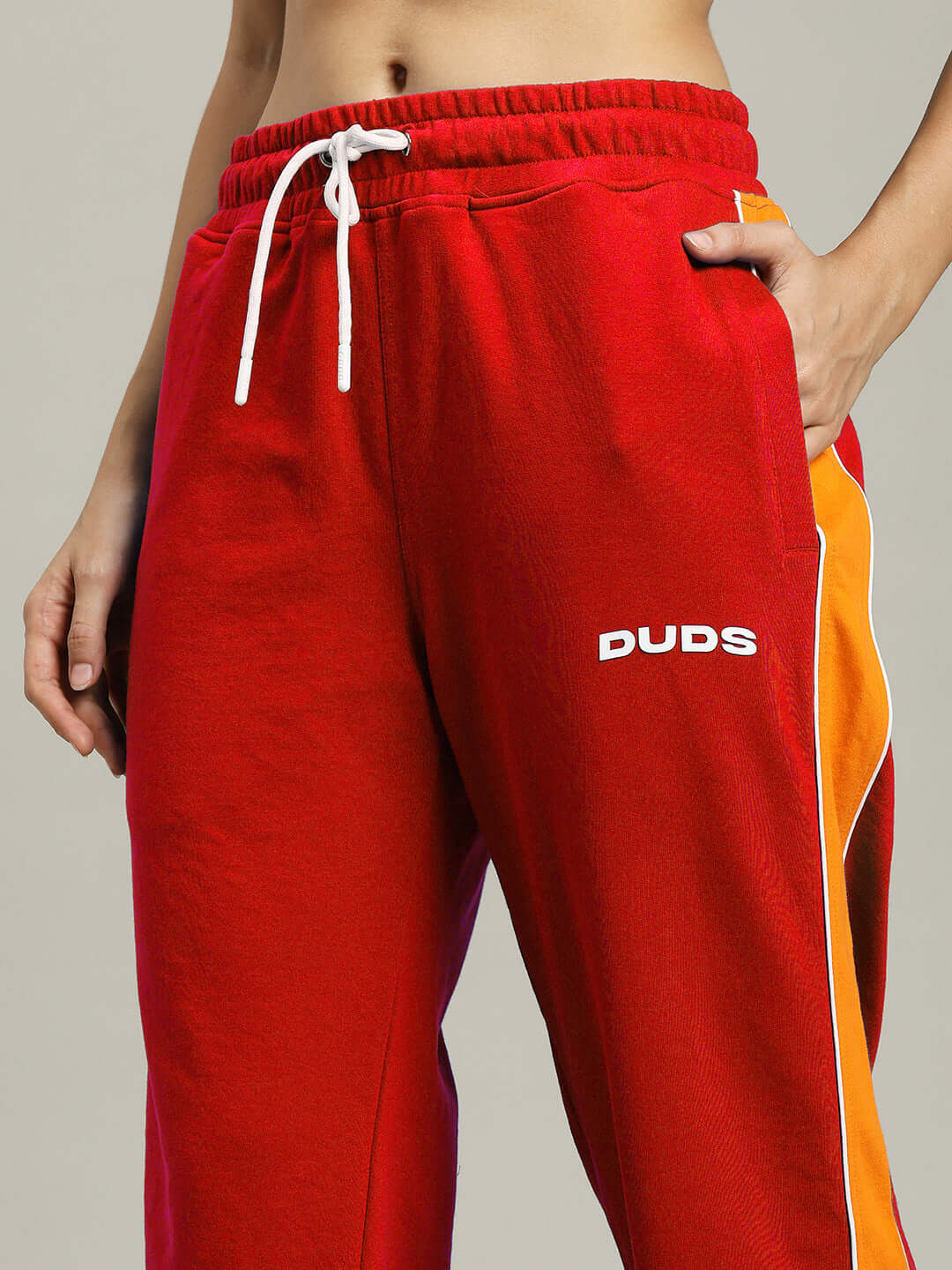 Woman wearing red Sanford Stripe Joggers with DUDS logo, featuring white drawstrings and orange side stripe design.
