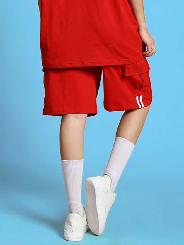 Woman wearing red Scotia regular fit shorts with white sneakers and socks, showcasing a stylish casual outfit against a blue background.