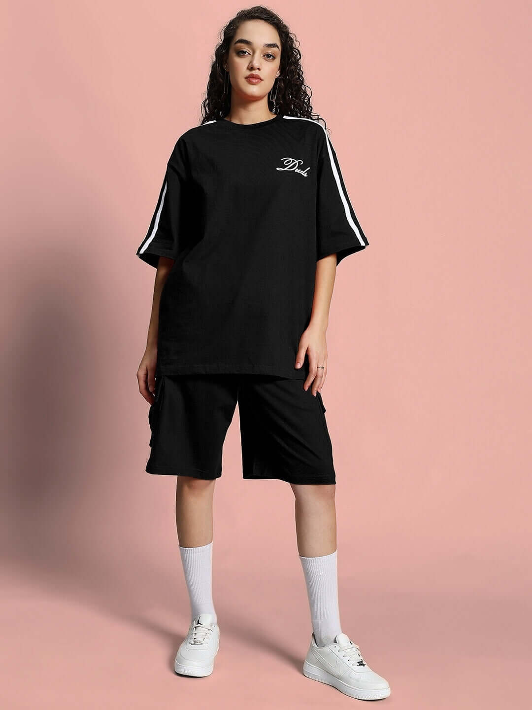 Woman wearing WOMEN'S SCOTIA SUMMER CO-ORD SET BLACK, showcasing chic minimalist style on a pink background.