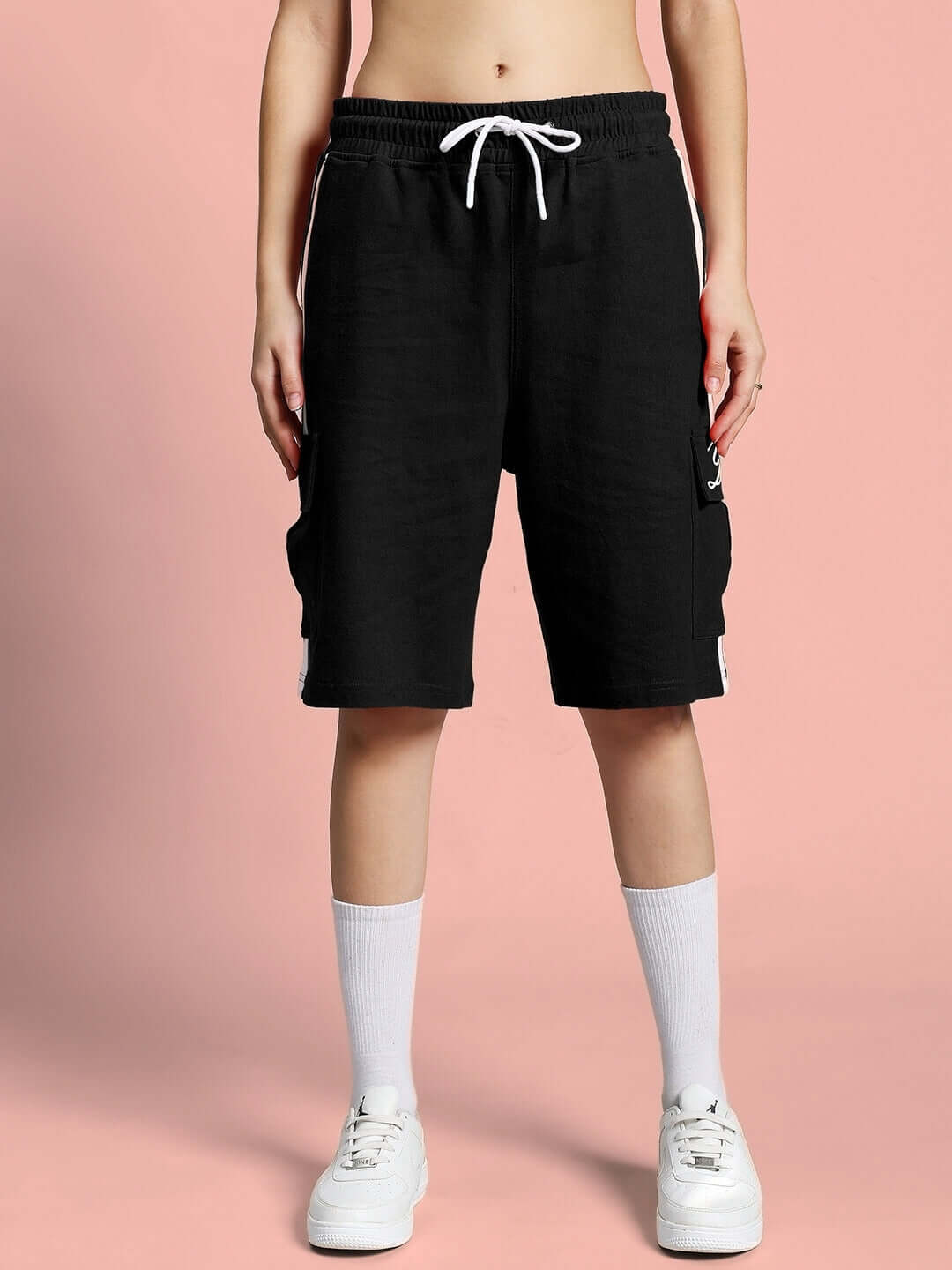 Model wearing WOMEN'S SCOTIA SUMMER CO-ORD SET BLACK shorts with white sneakers on pink background.