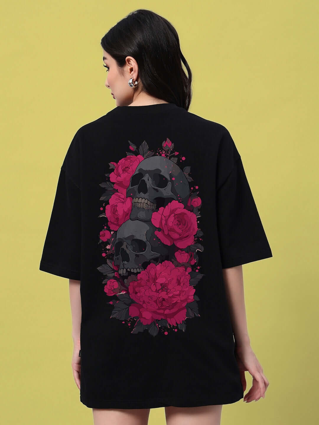Back view of a woman wearing a black oversized t-shirt featuring a vibrant skull and roses design, perfect for trendy summer style.
