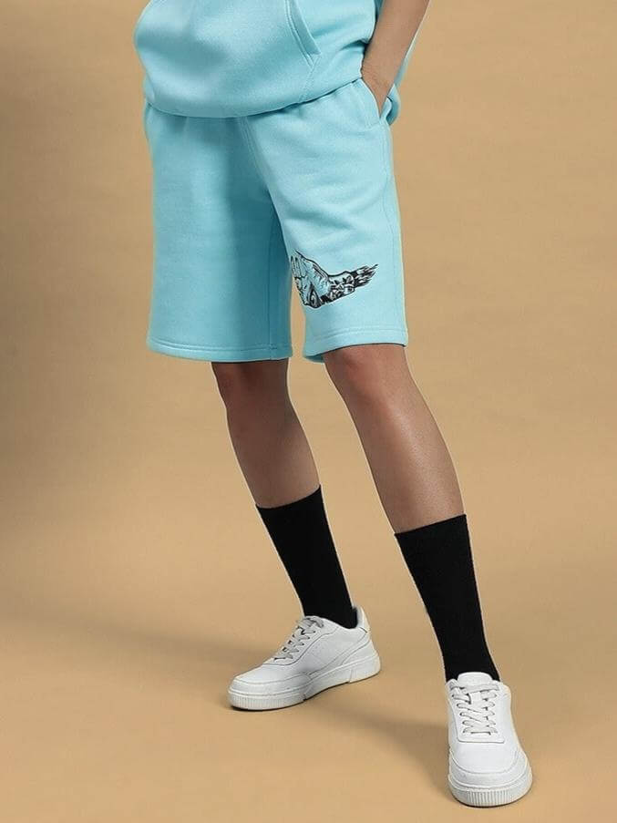 Person wearing WOMEN DEMON FLEECE SHORTS SKY BLUE with design, standing on beige background.