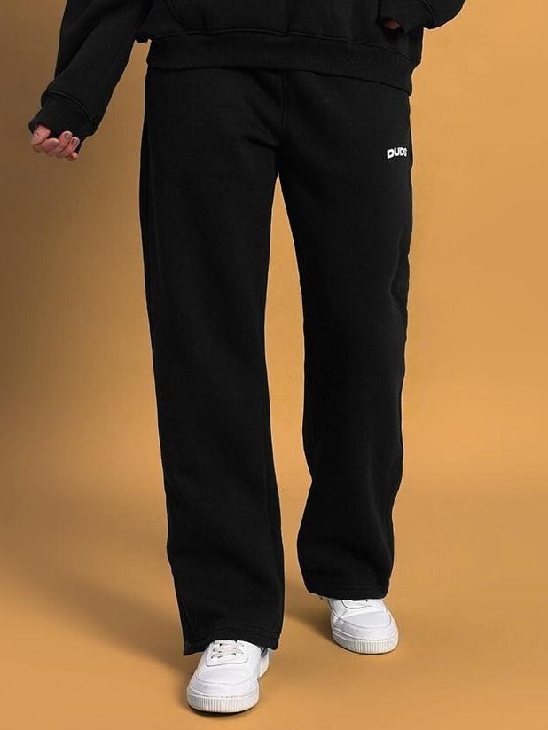 Woman wearing WOMEN'S SOOTY FLEECE CARGO PANT BLACK with white sneakers on beige background.