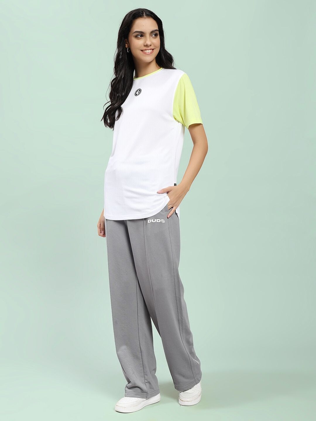 Woman wearing WOMEN SPIRAL RELAXED-FIT JOGGERS GREY with casual white and lime green t-shirt, standing against a pastel background.