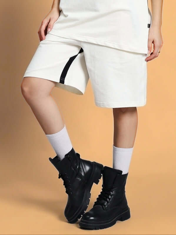 A person wearing off-white women's splinter regular fit shorts paired with black boots and white socks, standing on a beige background.