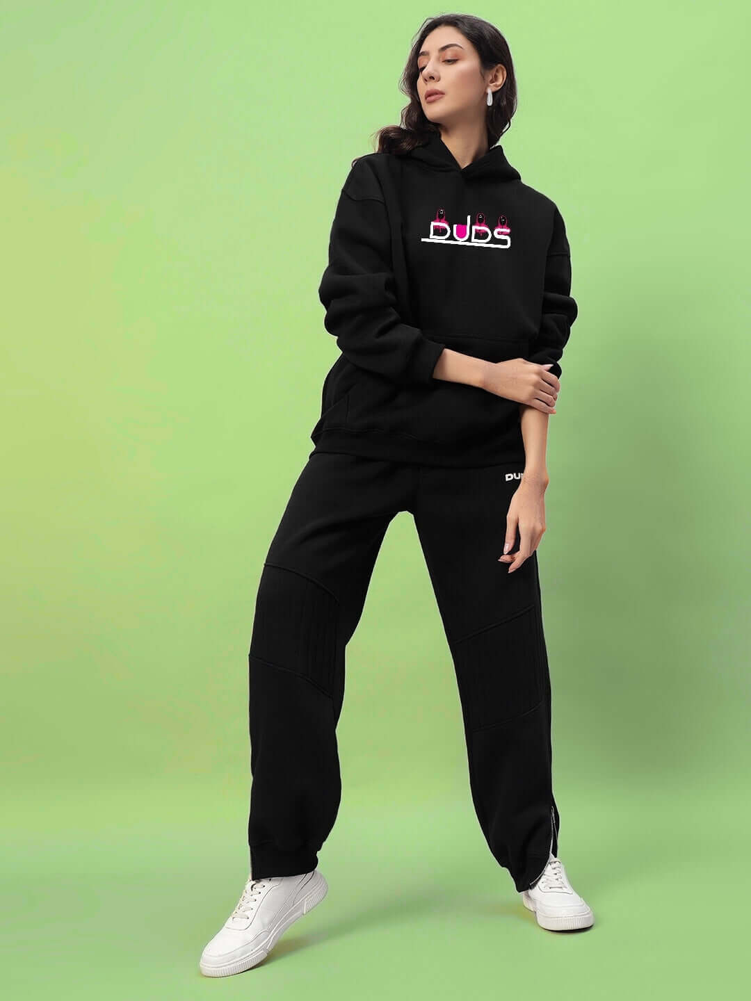 Model wearing WOMENS SQUID GAME OVERSIZED HOODIE BLACK, standing against a green background, showcasing bold streetwear style.