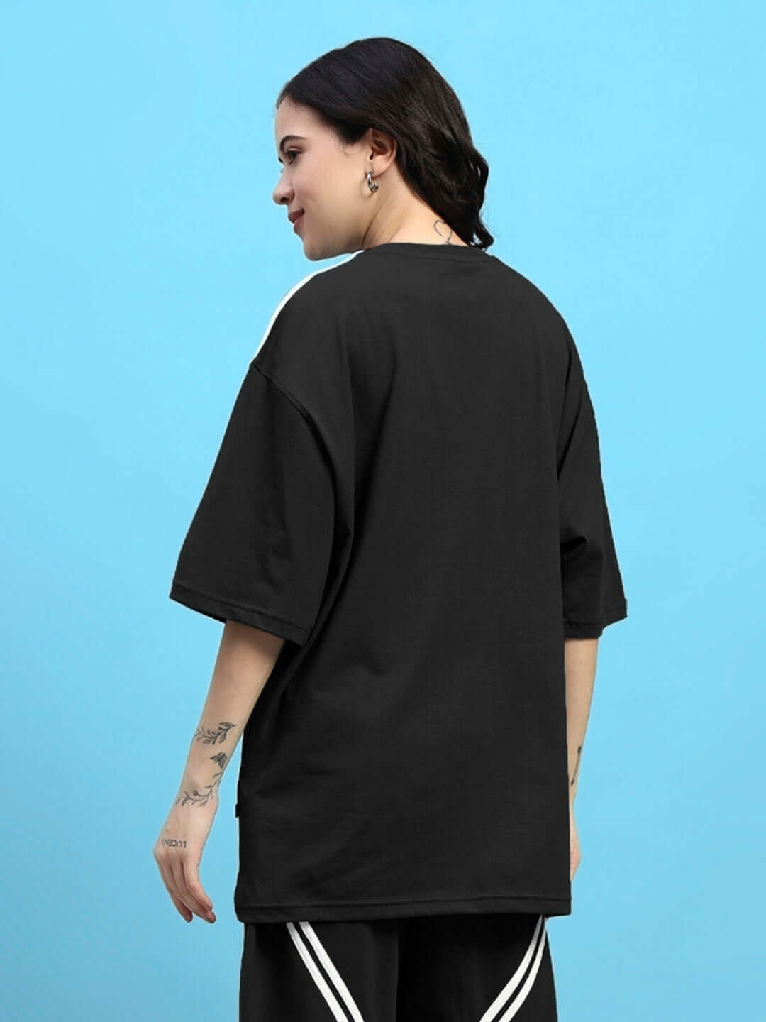 Rear view of a woman wearing a black oversized t-shirt made from premium cotton, featuring a relaxed fit and stylish design.