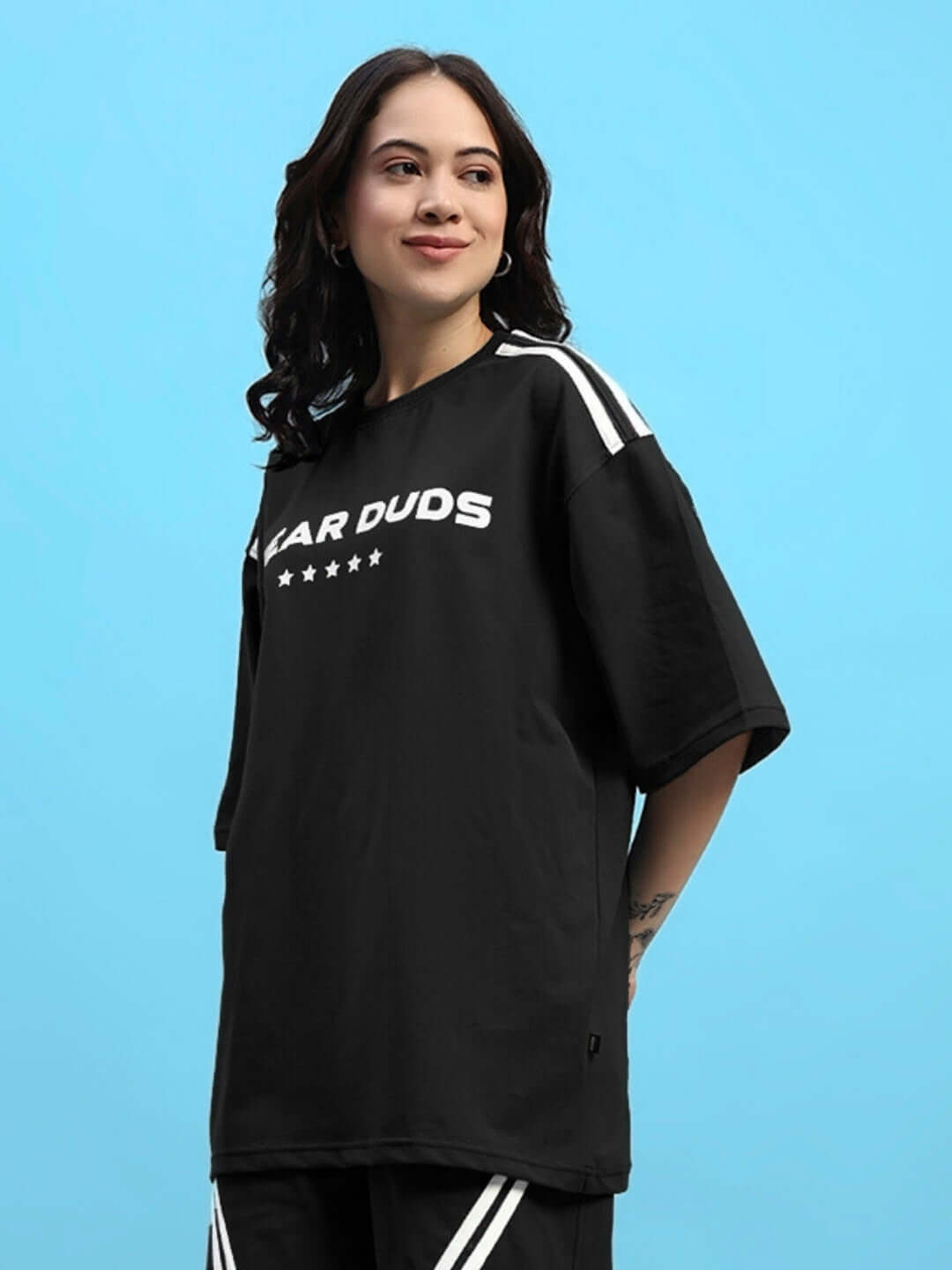 Woman wearing an oversized black t-shirt with star design, made from premium cotton blend fabric, 220 GSM, in front of a blue background.