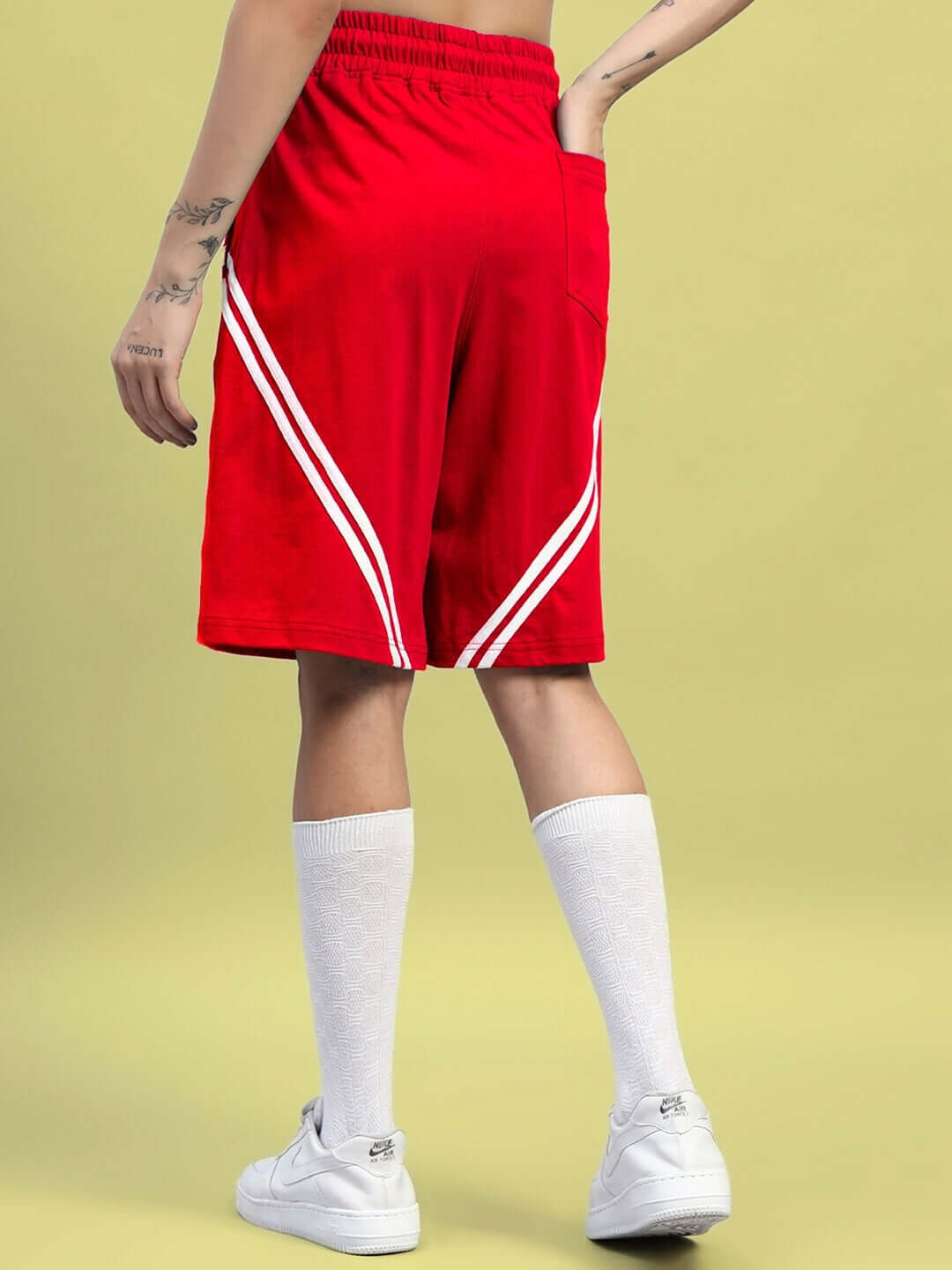 Woman wearing red Women's Star Jumper Regular Fit Shorts with white athletic shoes and knee-high socks on a yellow background.