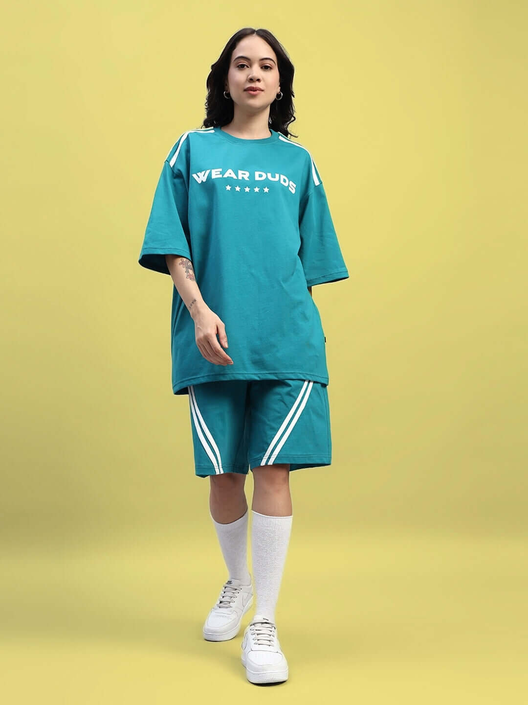 Model wearing WOMEN'S STAR JUMPER REGULAR FIT SHORTS TEAL with matching teal top against yellow background.
