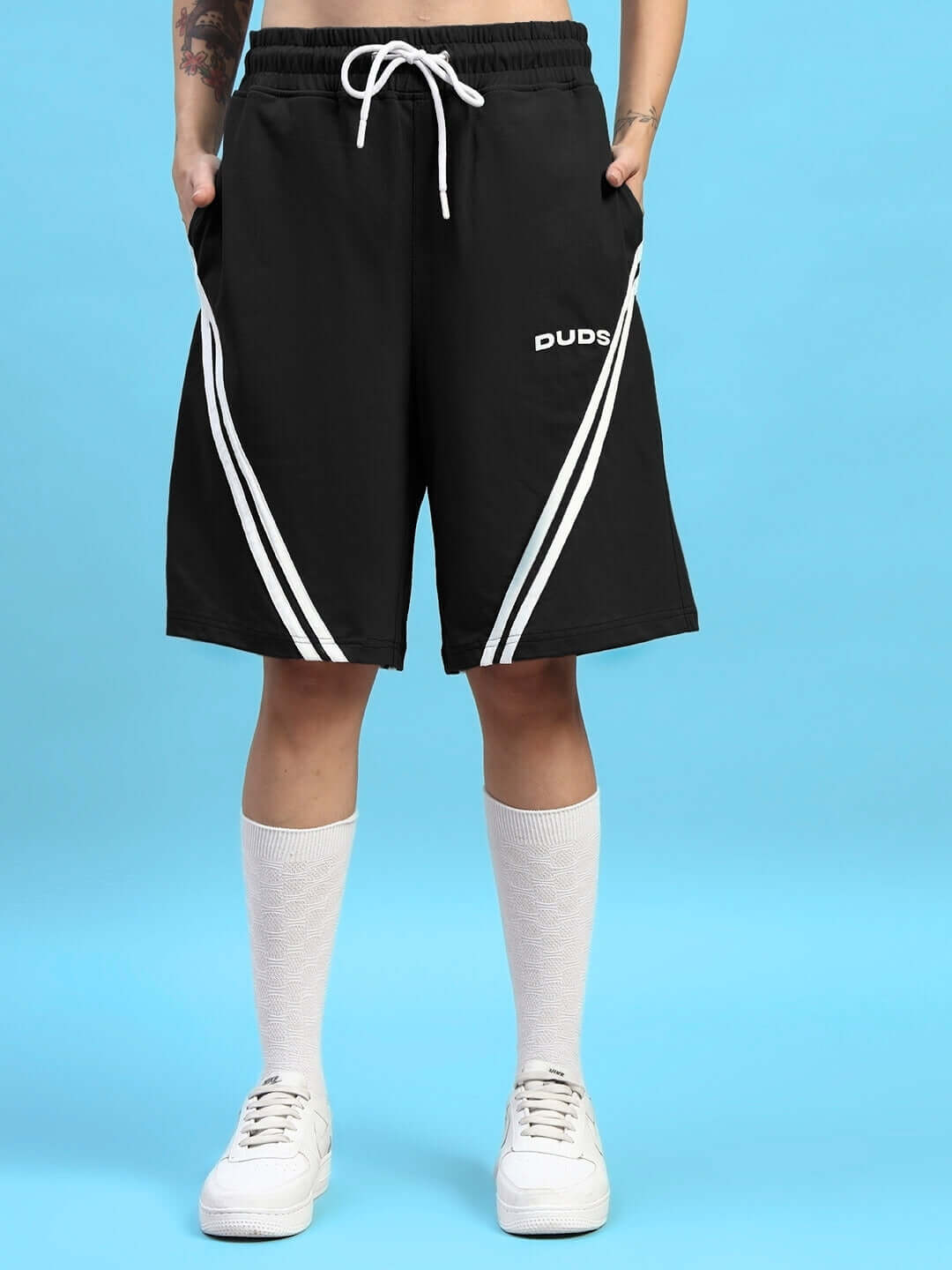 Black athletic shorts with white stripes and 'DUD S' logo, worn by a person standing against a blue background.