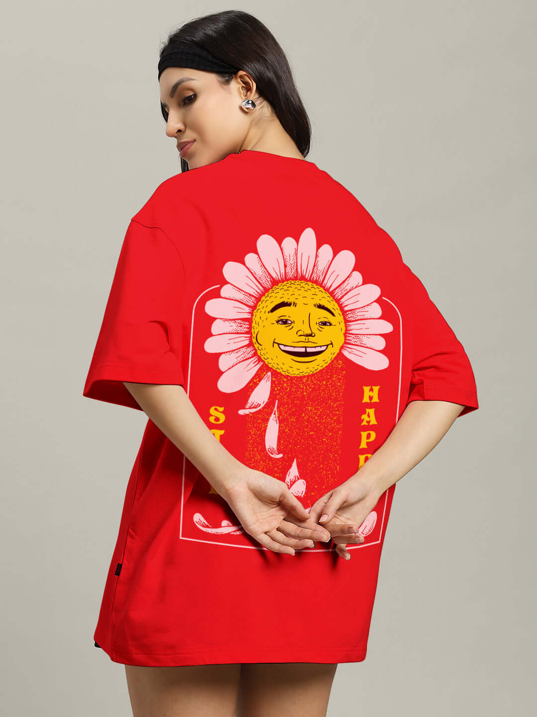Back view of woman wearing a red oversized T-shirt with a smiling sun print and the words 'Stay Happy', made from premium cotton blend.