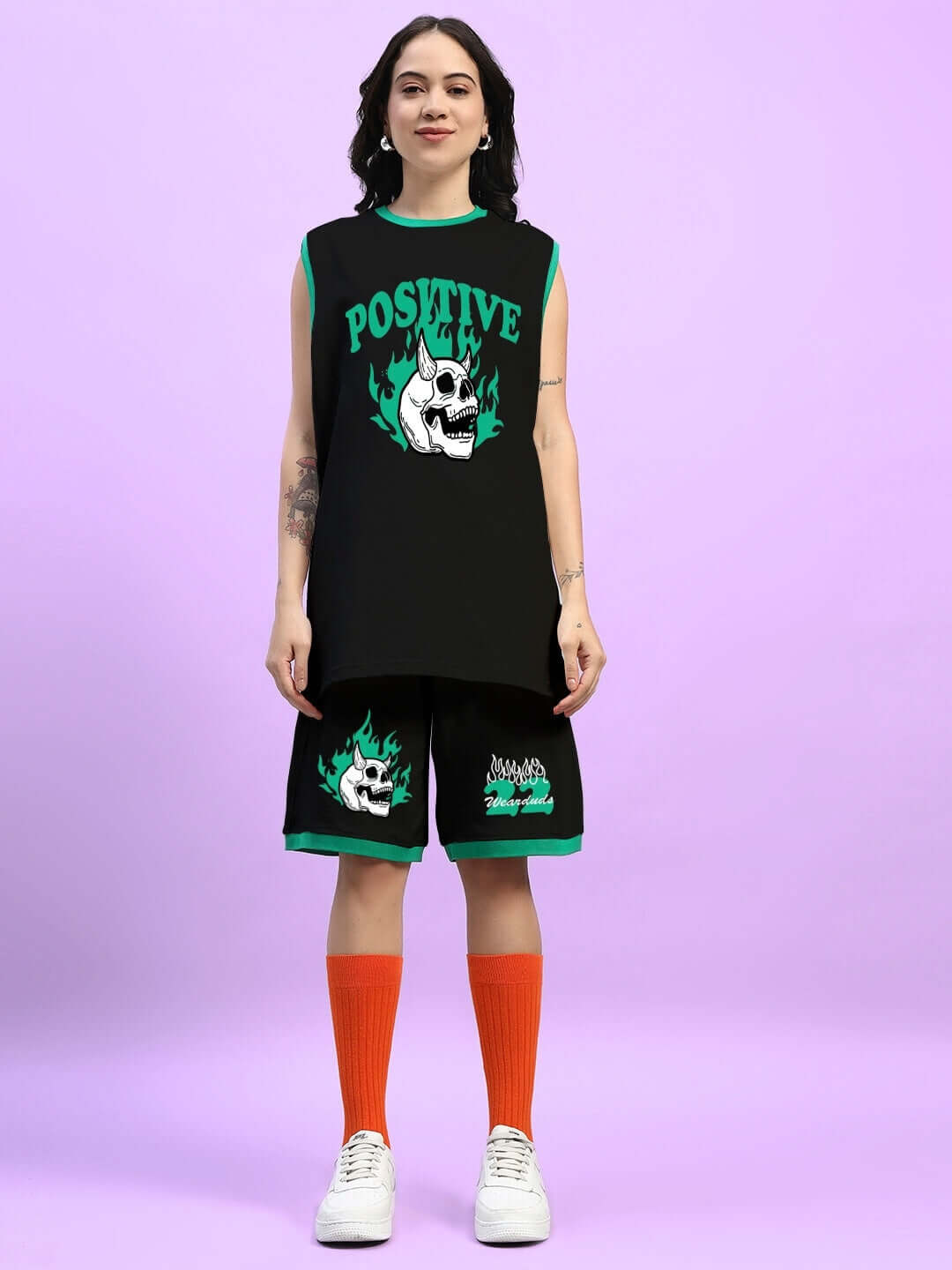 Woman wearing black 'Stay Positive' co-ord set with skull graphic, orange socks, and white sneakers.