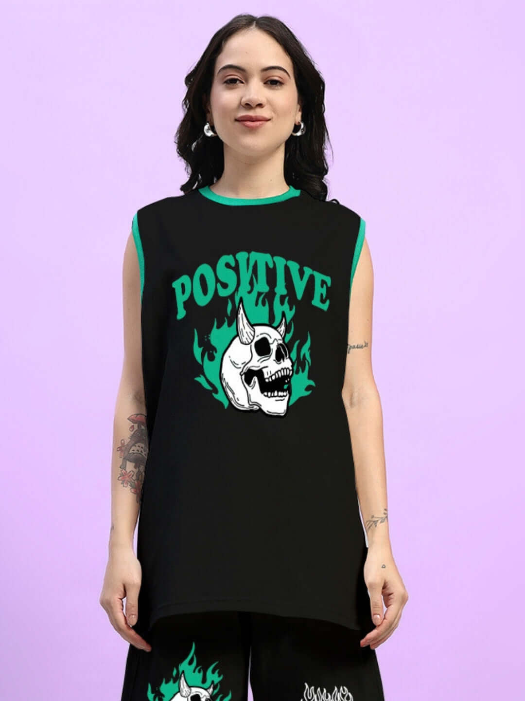 Woman wearing a black oversized t-shirt with 'Stay Positive' skull design, paired with matching shorts against a purple background.