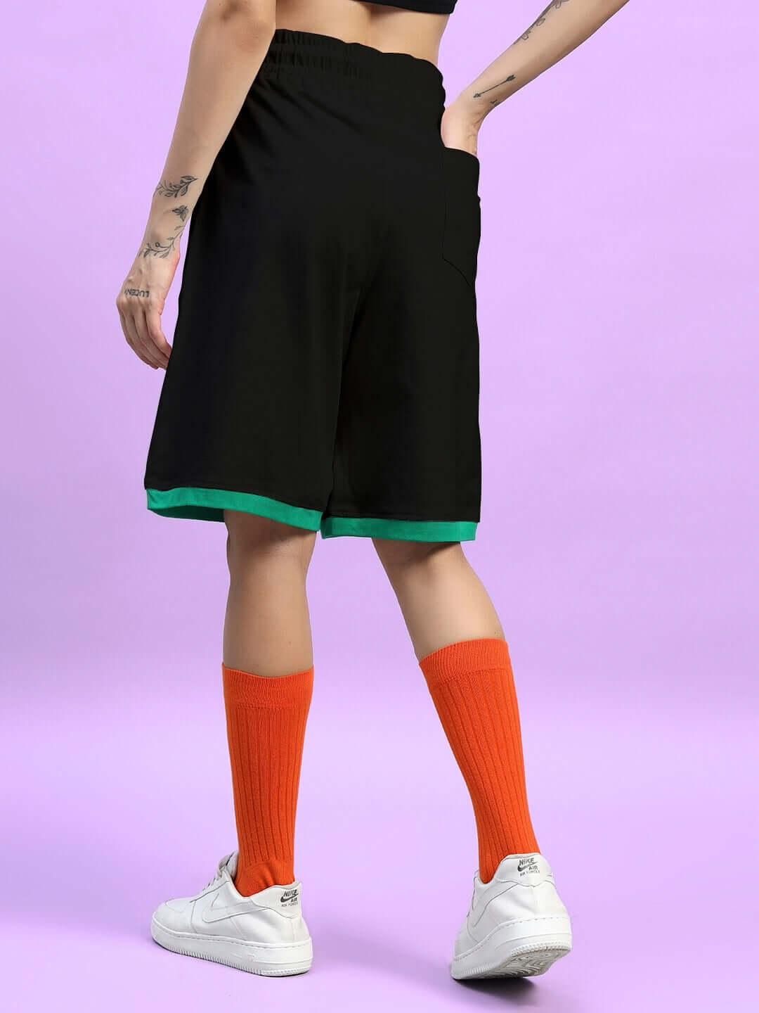 Back view of women's black Stay Positive summer shorts, paired with bright orange socks and white sneakers.