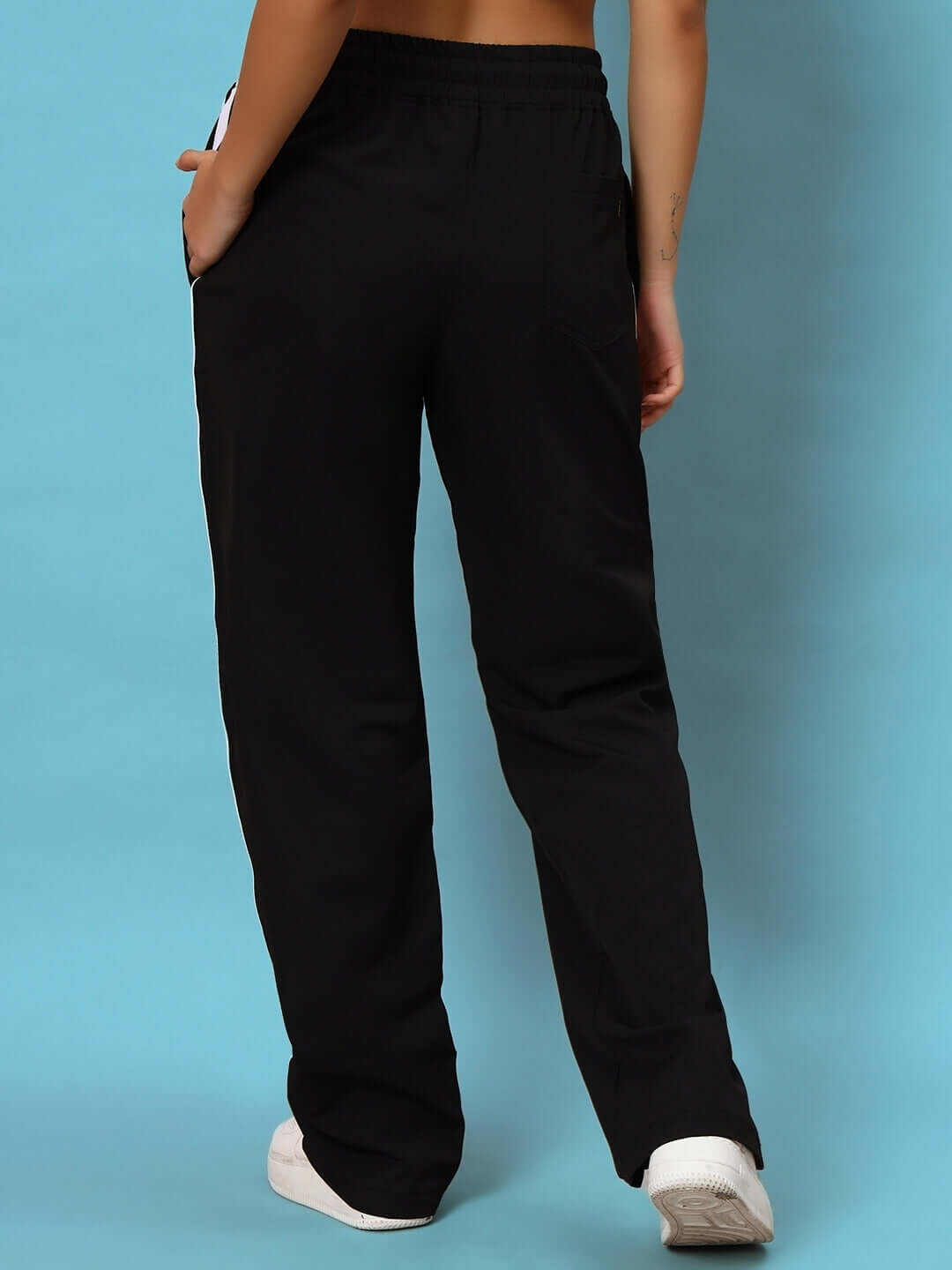 Back view of women's black string parachute cargo pants with hands in pockets against a blue background.