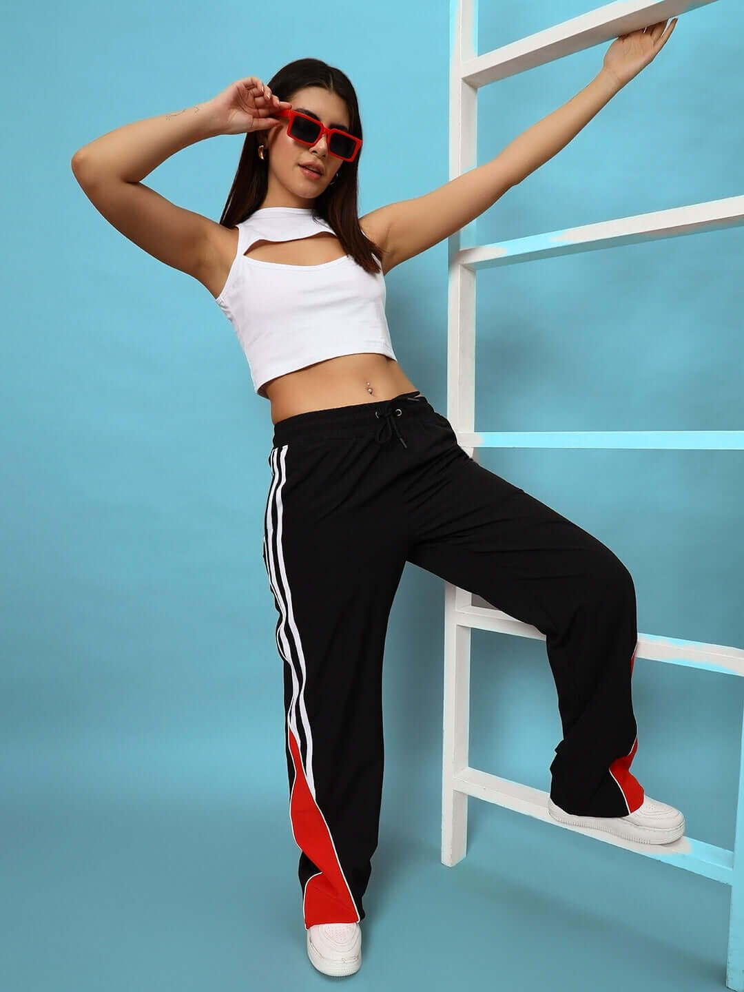 Model wearing women's string parachute cargo pants in black with a white top, posing against a blue background with a ladder.