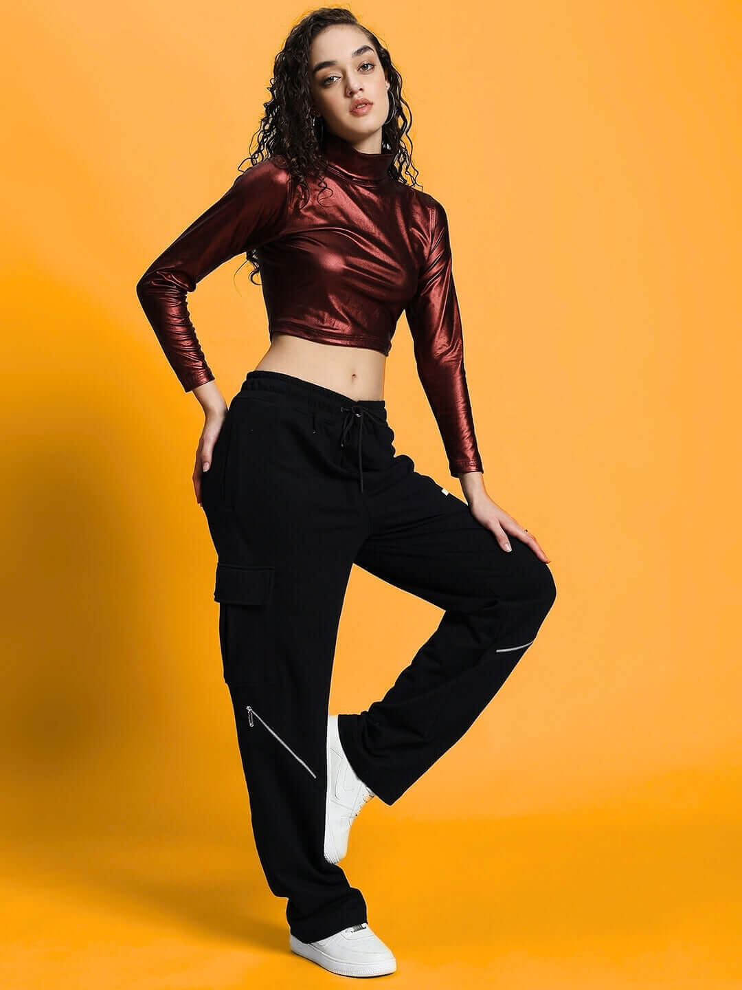 Woman wearing maroon metallic crop top and black pants against yellow background. Stylish and chic fashion.
