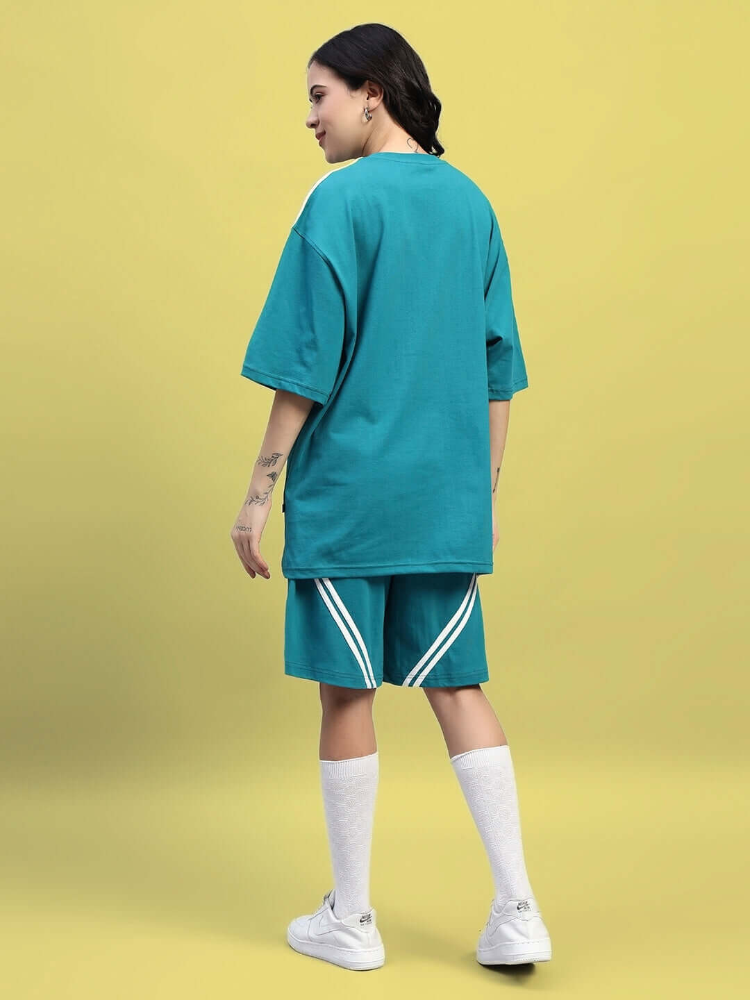 Model wearing WOMEN'S STAR JUMPER OVER-SIZED T-SHIRT TEAL showcasing back view on yellow background.