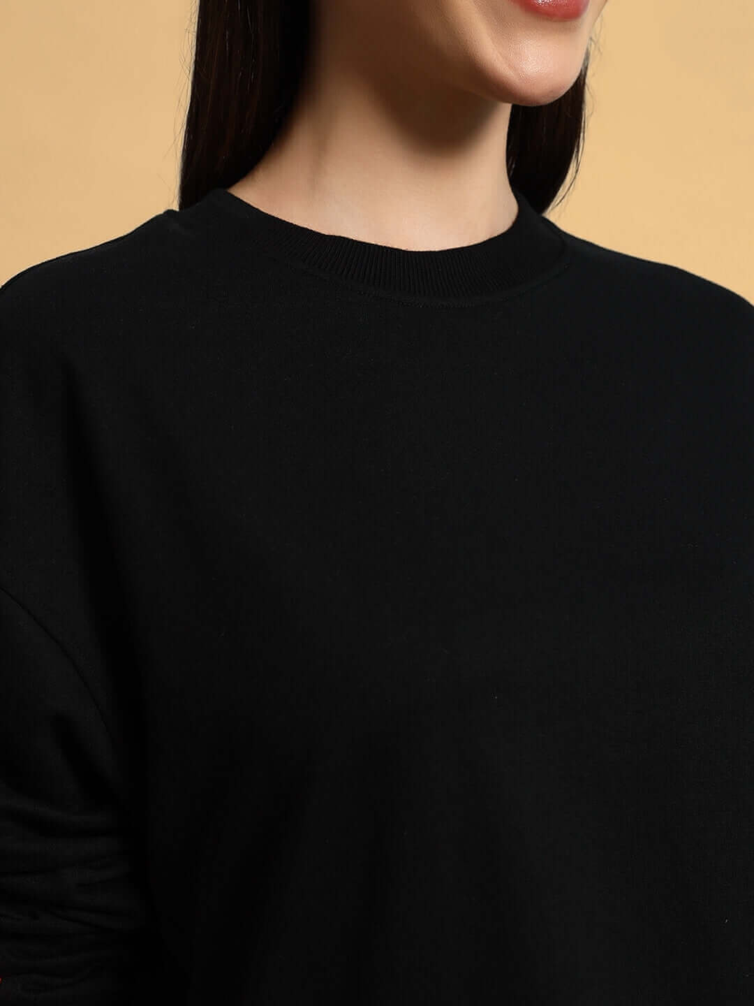 Close-up of a woman wearing a black oversized sweatshirt made of premium cotton French terry with a round neckline.