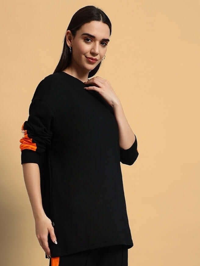 Woman wearing a black oversized sweatshirt with orange accents, made of premium cotton French Terry Lycra, showcasing casual fashion.