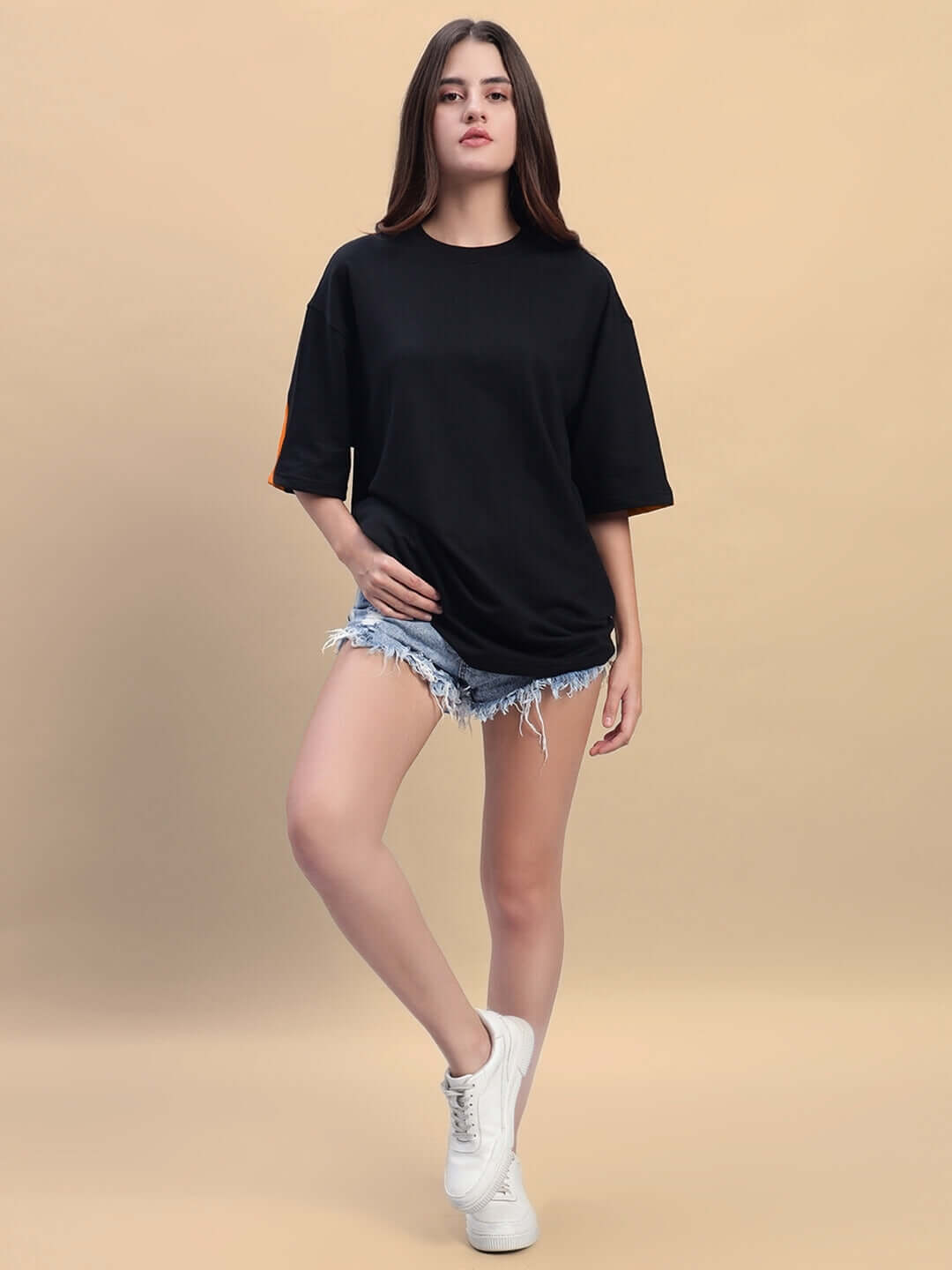 Woman wearing oversized black-orange women's Titan T-shirt, paired with denim shorts and white sneakers, showcasing casual street style.
