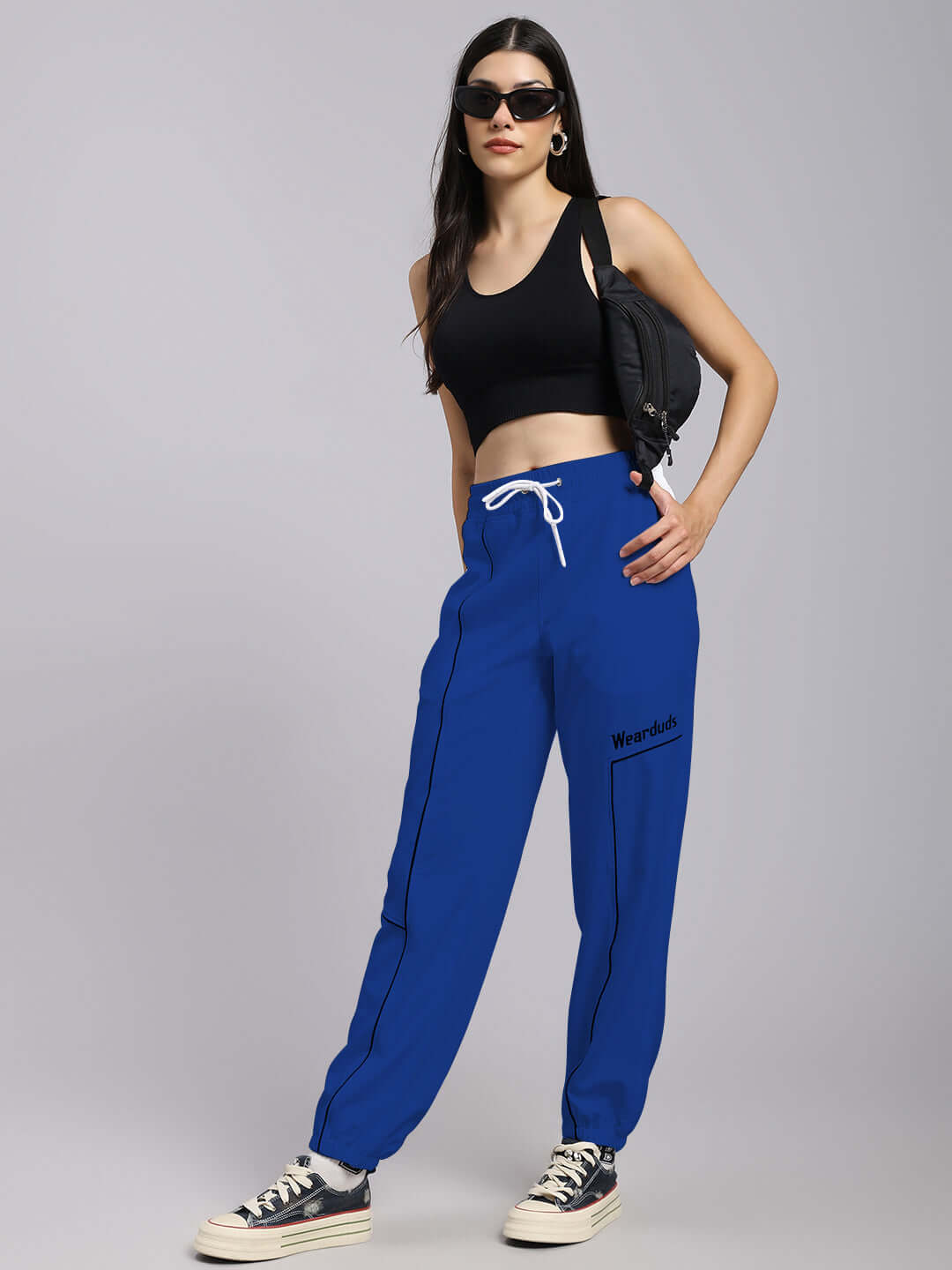 Model wearing Women's Tokyo Relaxed Fit Joggers in blue, paired with a black top and sneakers, showcasing a stylish casual look.